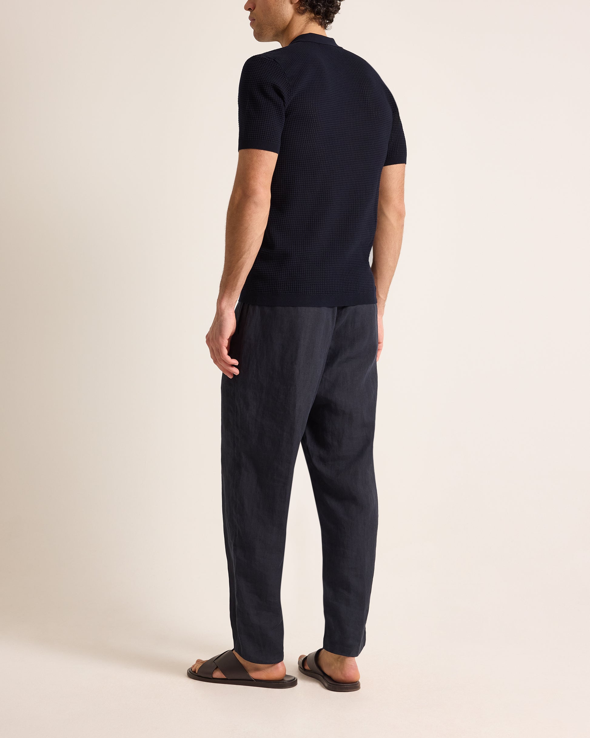 Man wearing a navy polo t-shirt and dark pants on a beige background