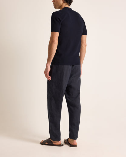 Man wearing a navy polo t-shirt and dark pants on a beige background