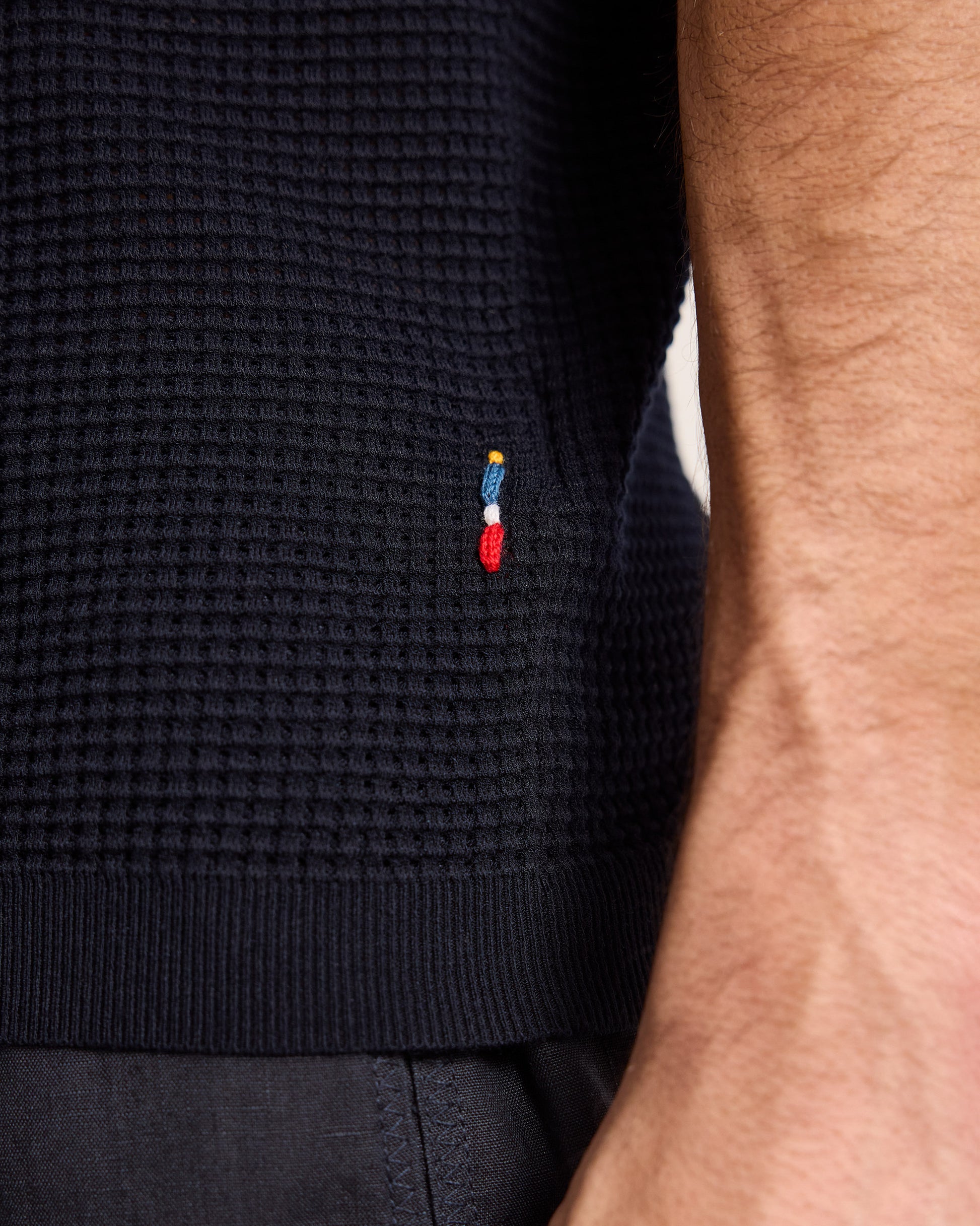 Close-up of a navy blue sweater with a small embroidered logo on a neutral background