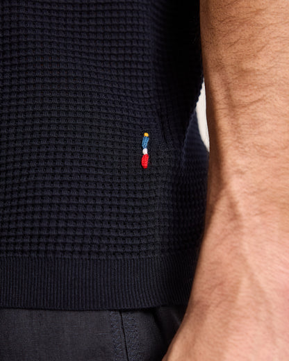 Close-up of a navy blue sweater with a small embroidered logo on a neutral background