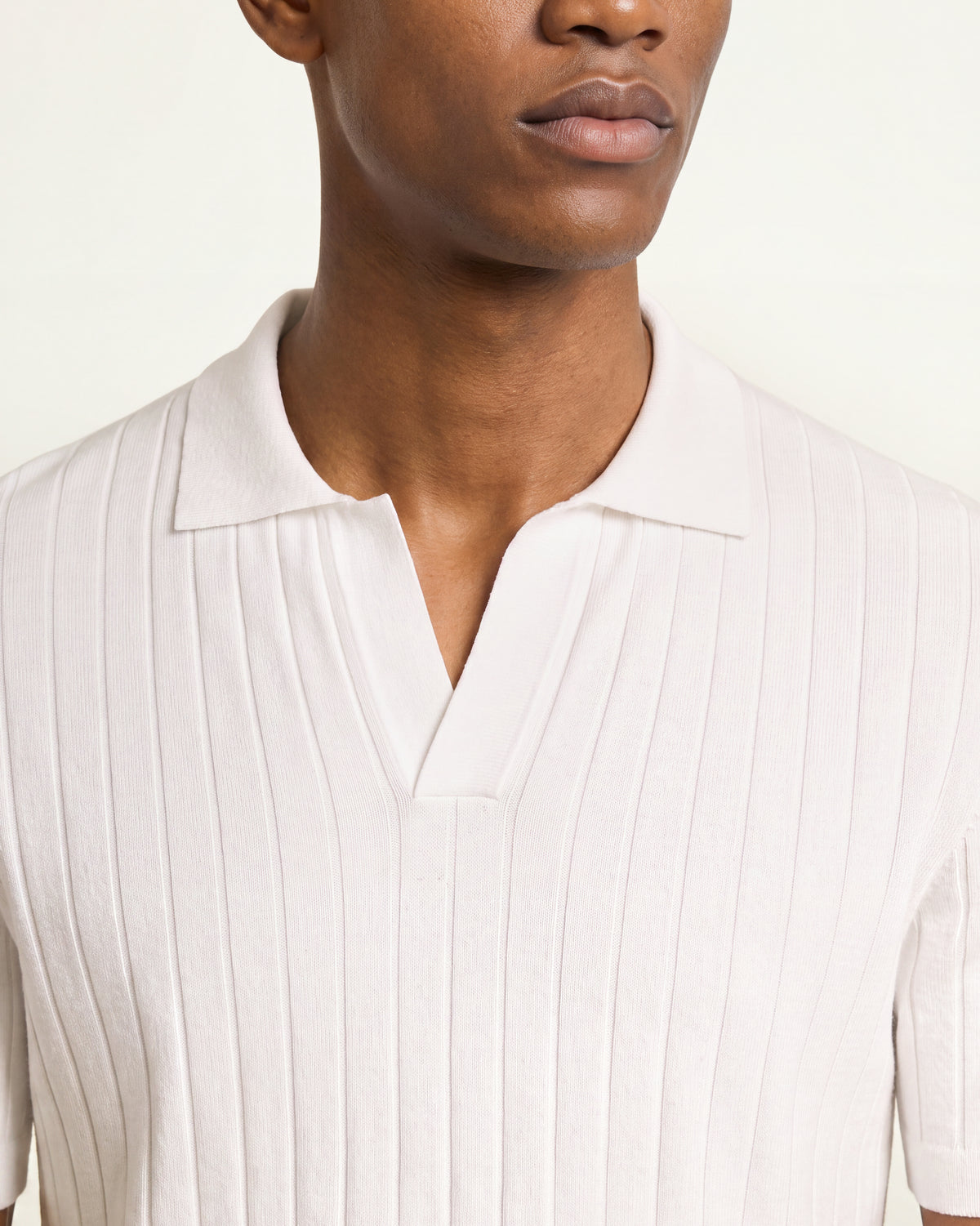 Close-up of a model wearing a white ribbed knit polo shirt with a split collar and split V-neck.