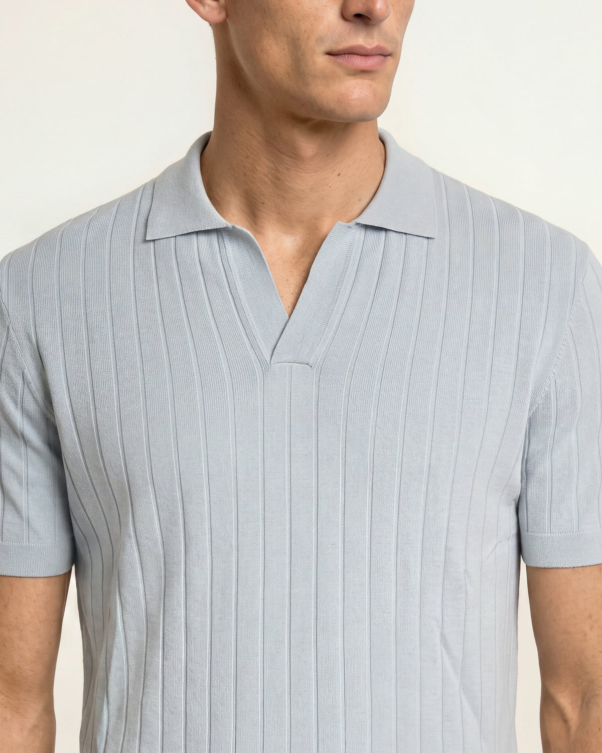 A close-up of a man wearing a light gray ribbed short-sleeve polo shirt against a plain off-white background.