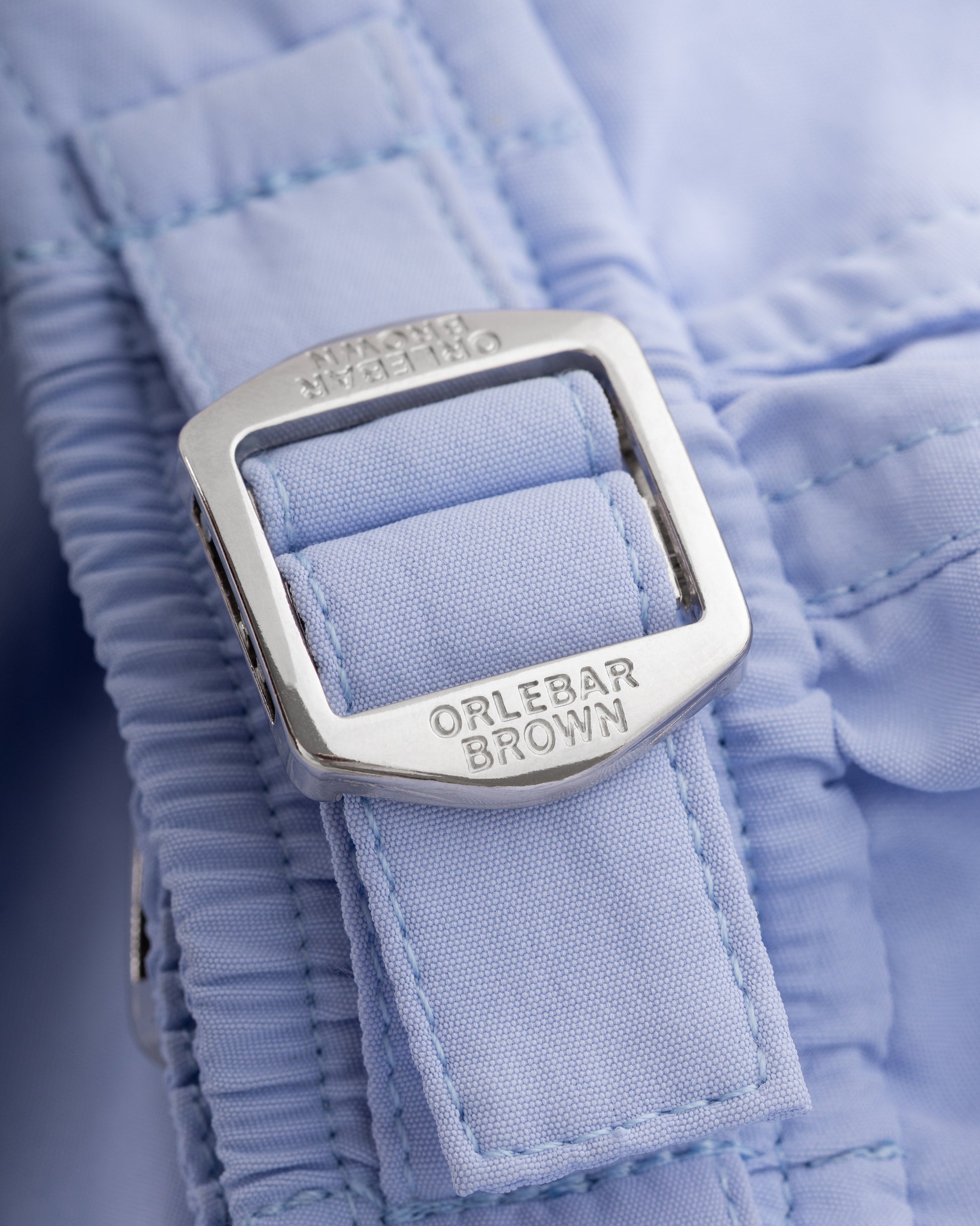 Close-up of a blue garment with a silver buckle and 'Orlebar Brown' branding.