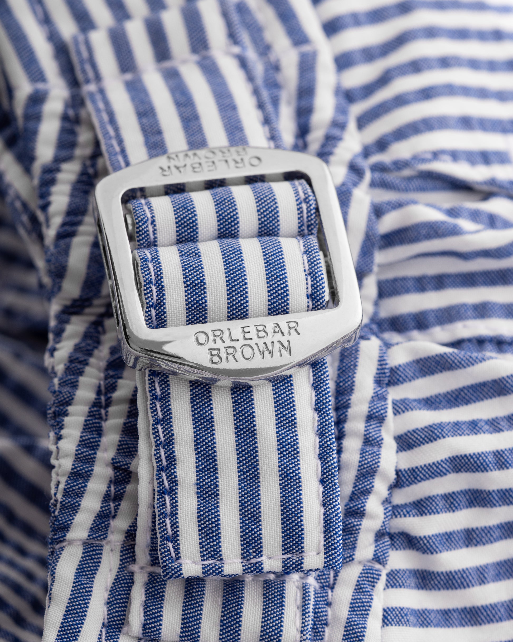 Close-up of a blue and white striped shirt with a visible Orlebar Brown belt buckle.