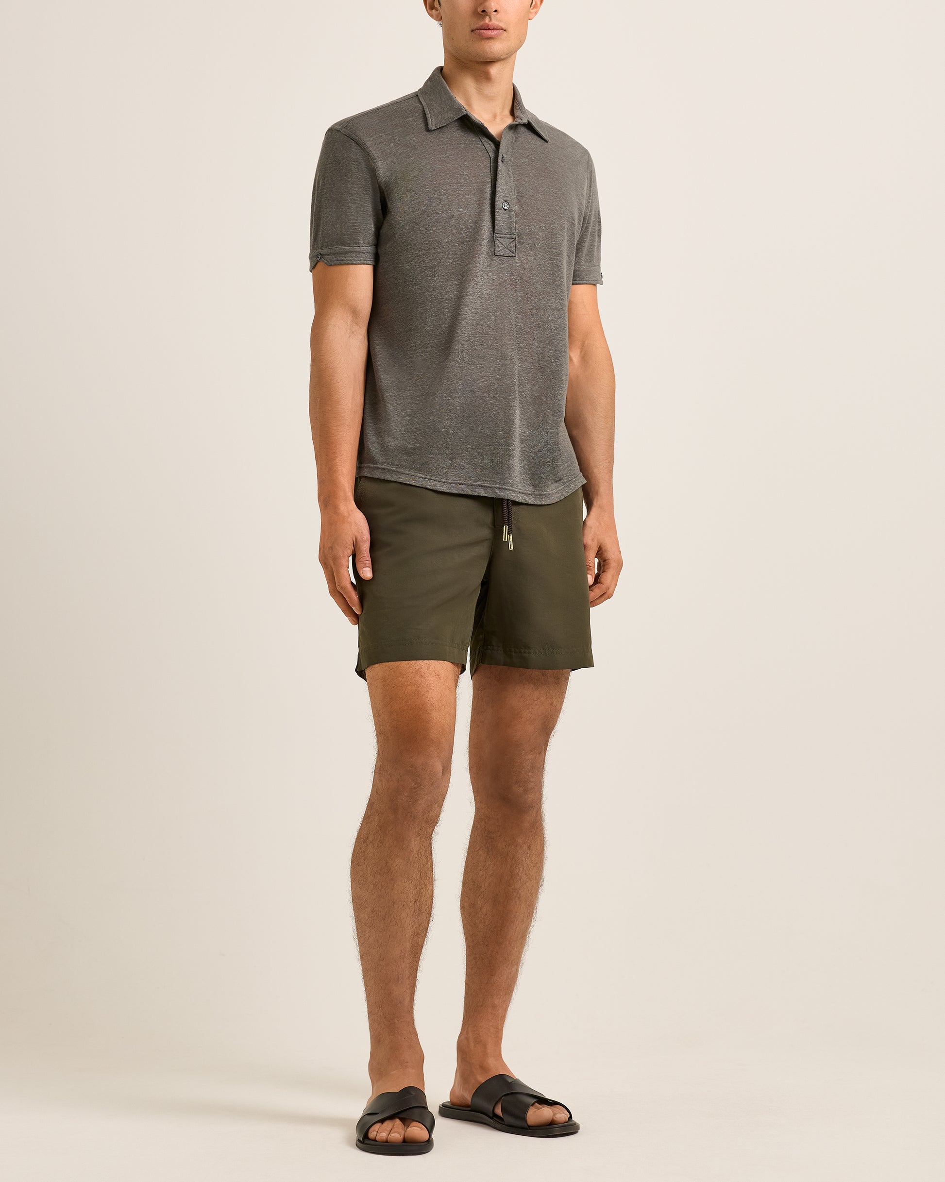 Person wearing a gray polo shirt and green shorts on a beige background