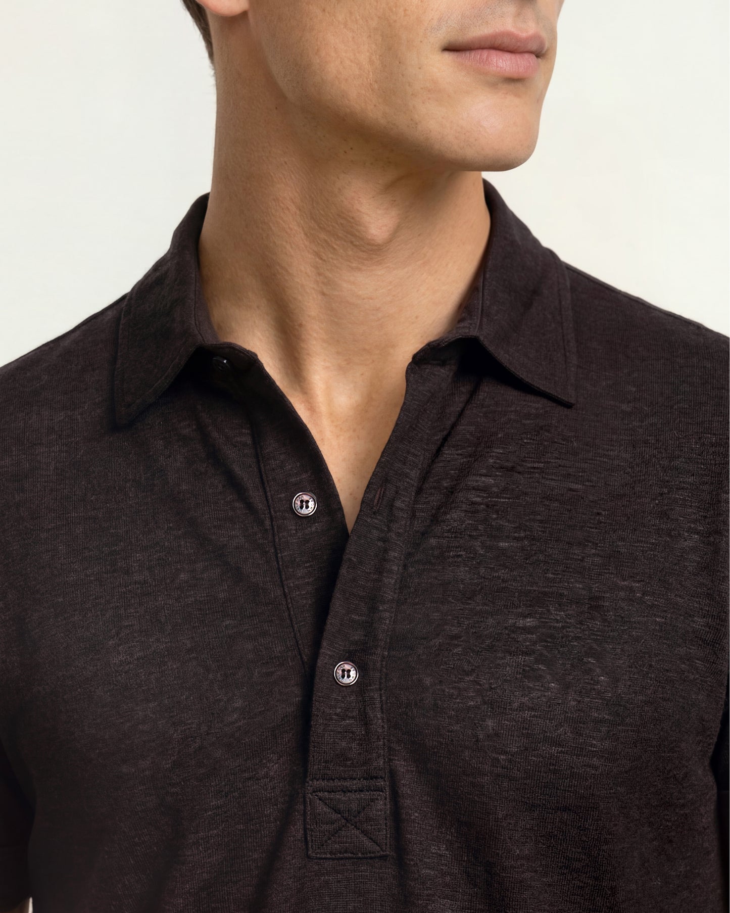 Close-up of a man wearing a dark brown heathered polo shirt with a buttoned collar and silver-toned buttons.