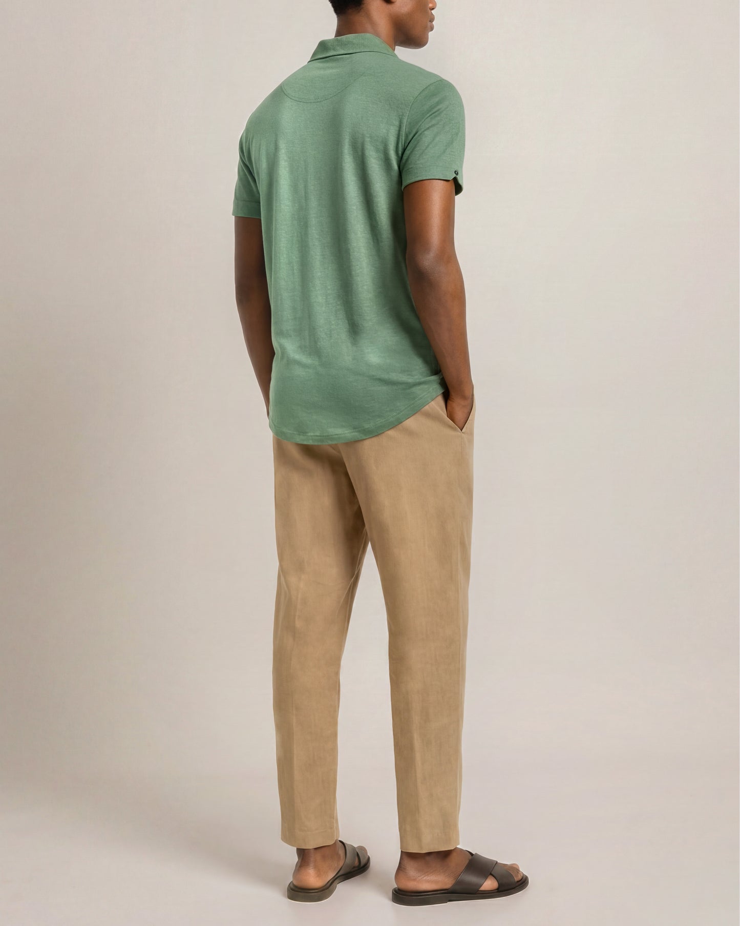 Man wearing a green polo shirt and beige pants against a plain background