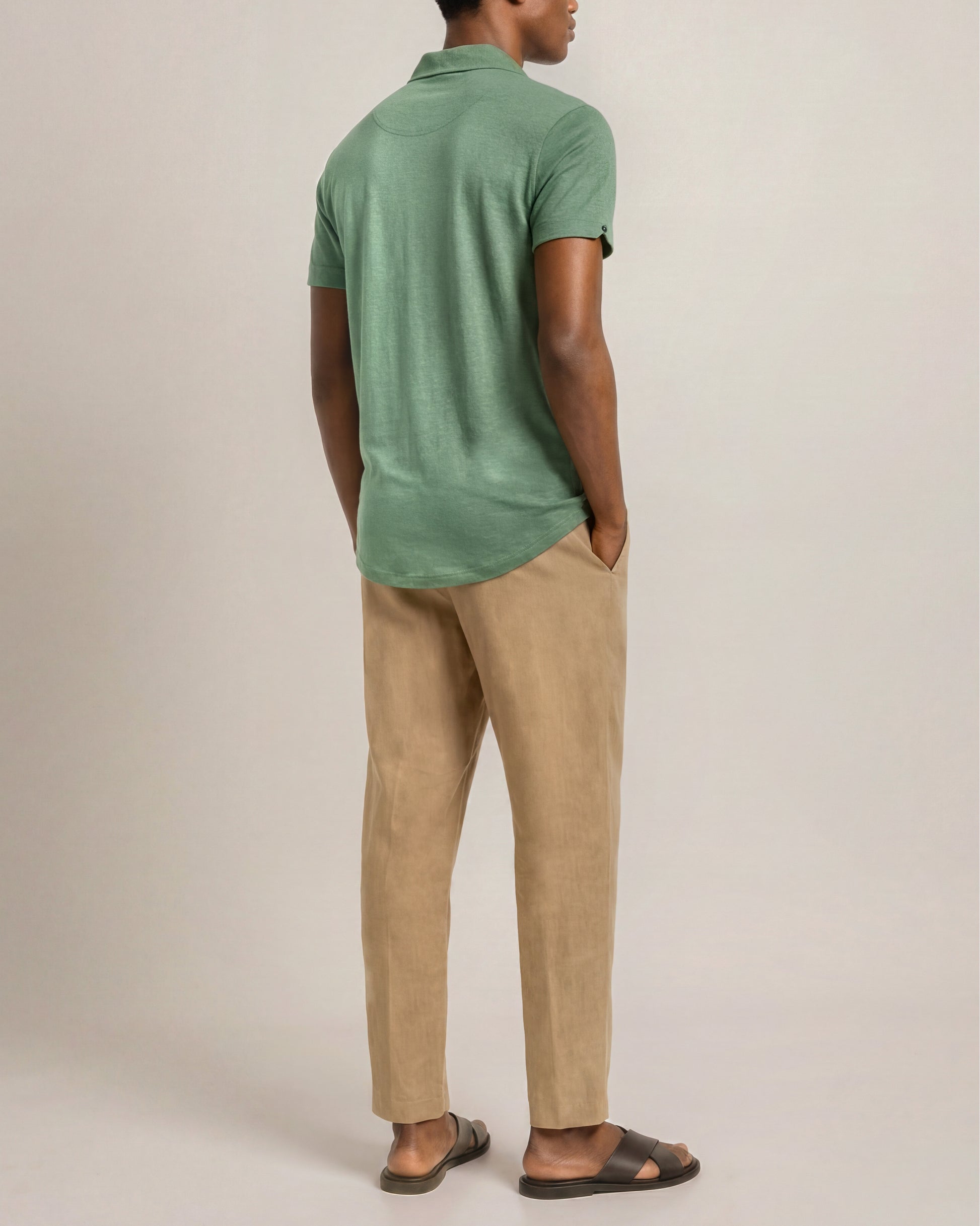 Man wearing a green polo shirt and beige pants against a plain background