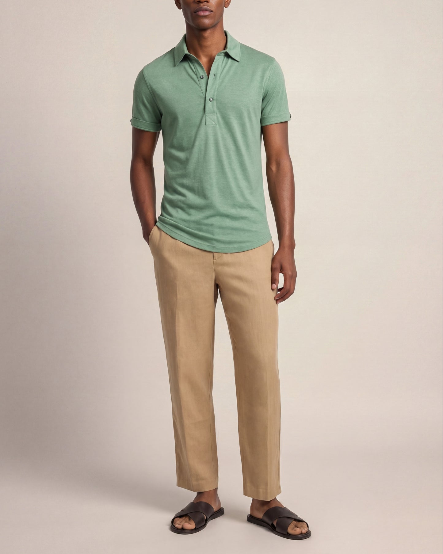Man wearing a green polo shirt and beige pants against a plain background