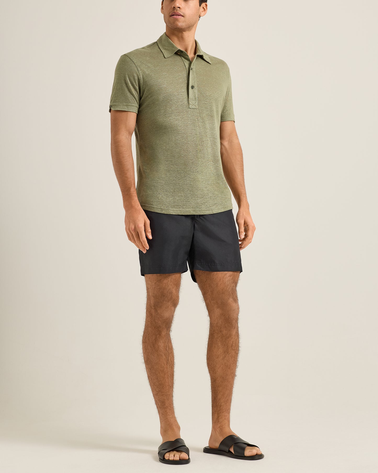 Man wearing a green polo shirt and black shorts on a plain background