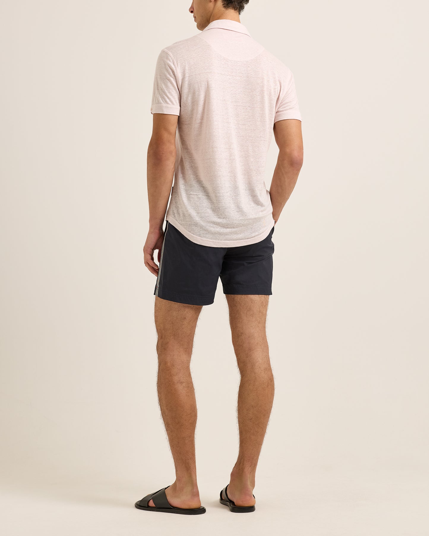 Man wearing a light-colored polo shirt and dark shorts on a plain background
