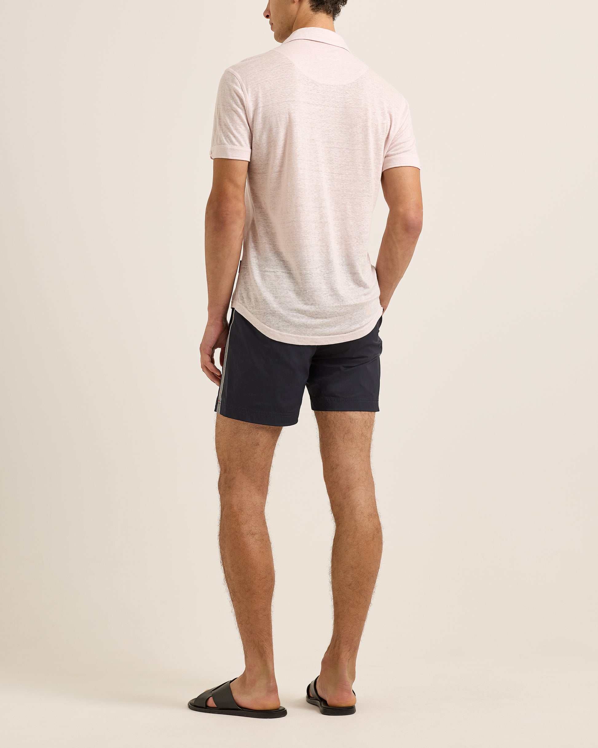 Man wearing a light-colored polo shirt and dark shorts on a plain background