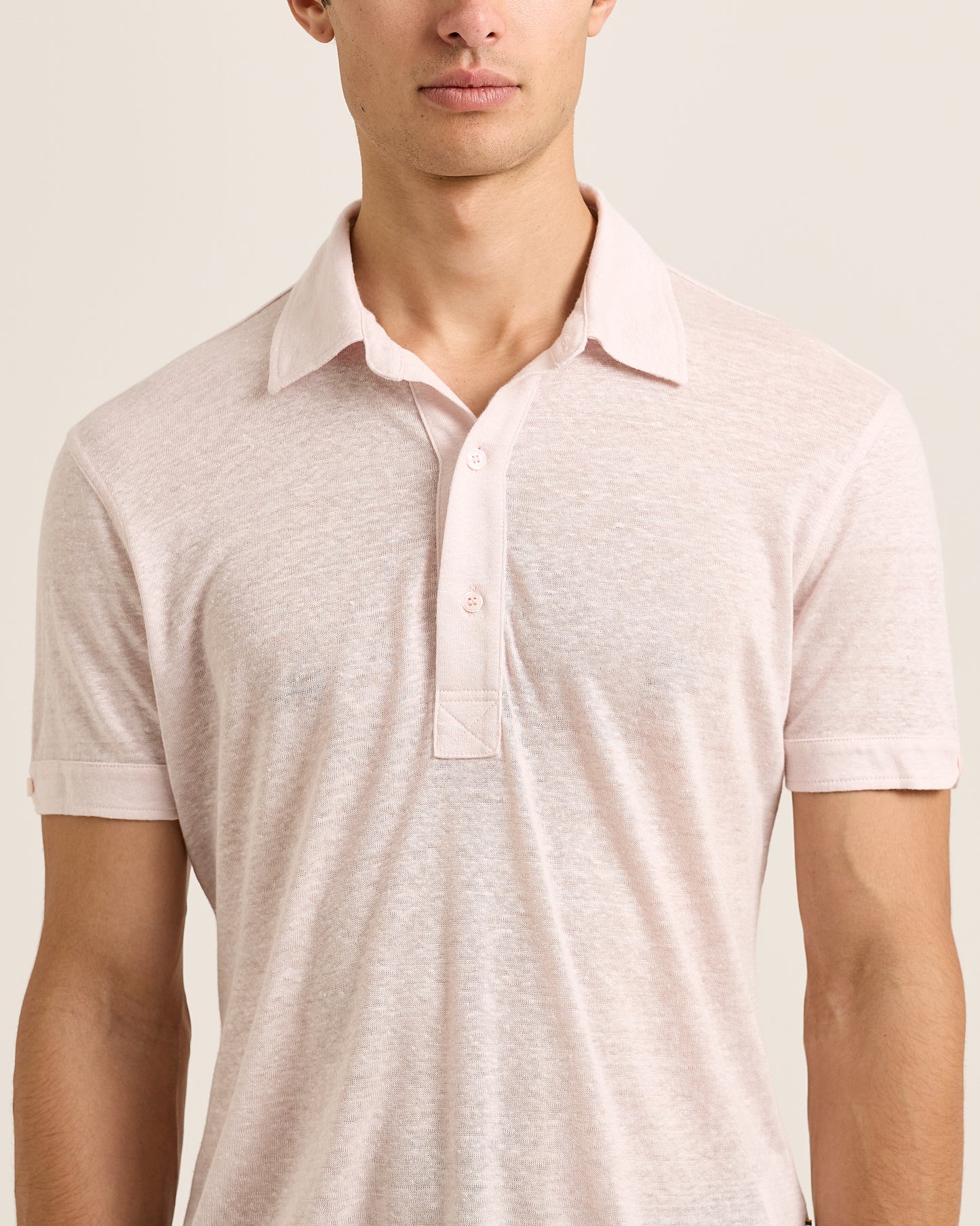 Man wearing a light pink polo shirt on a plain background