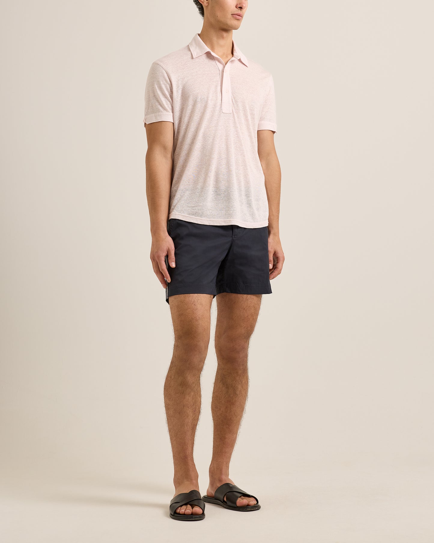 Man wearing a light pink polo shirt and dark shorts on a beige background