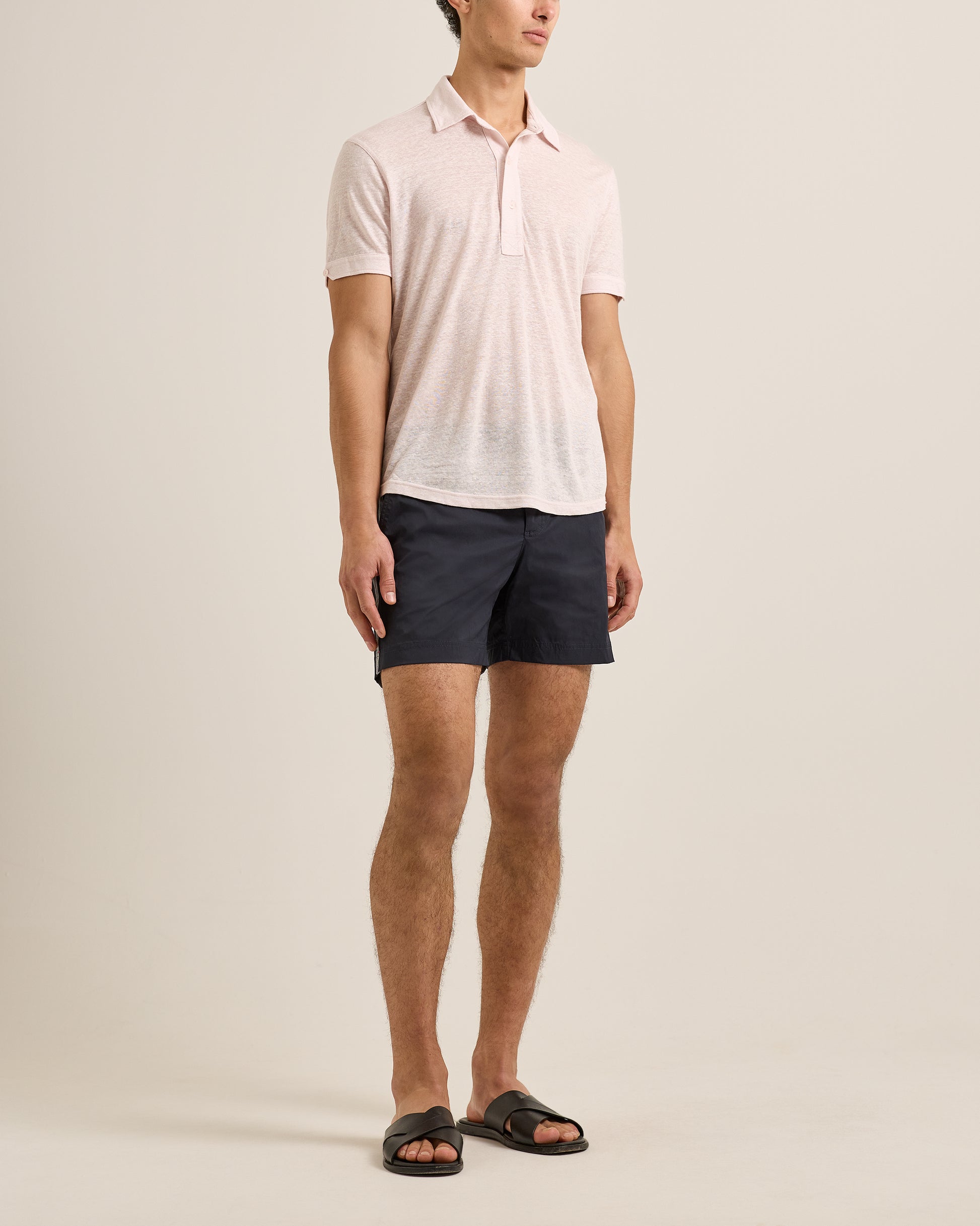 Man wearing a light pink polo shirt and dark shorts on a beige background