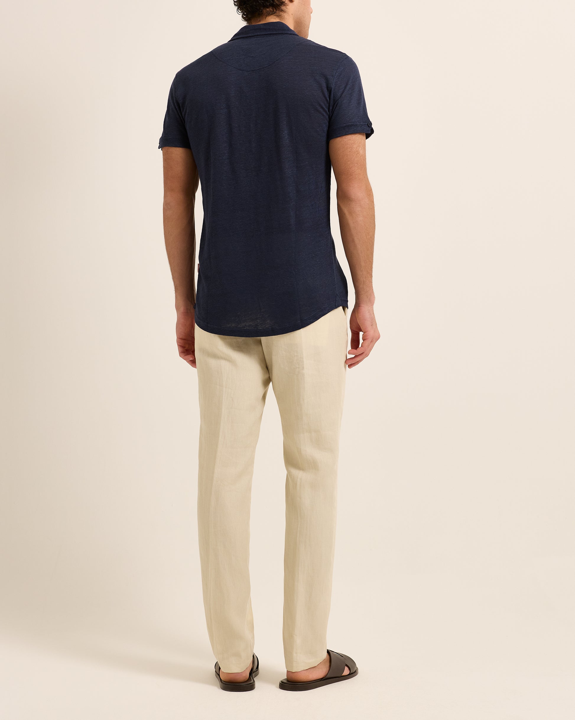 Man wearing navy polo shirt with beige trousers on a white background