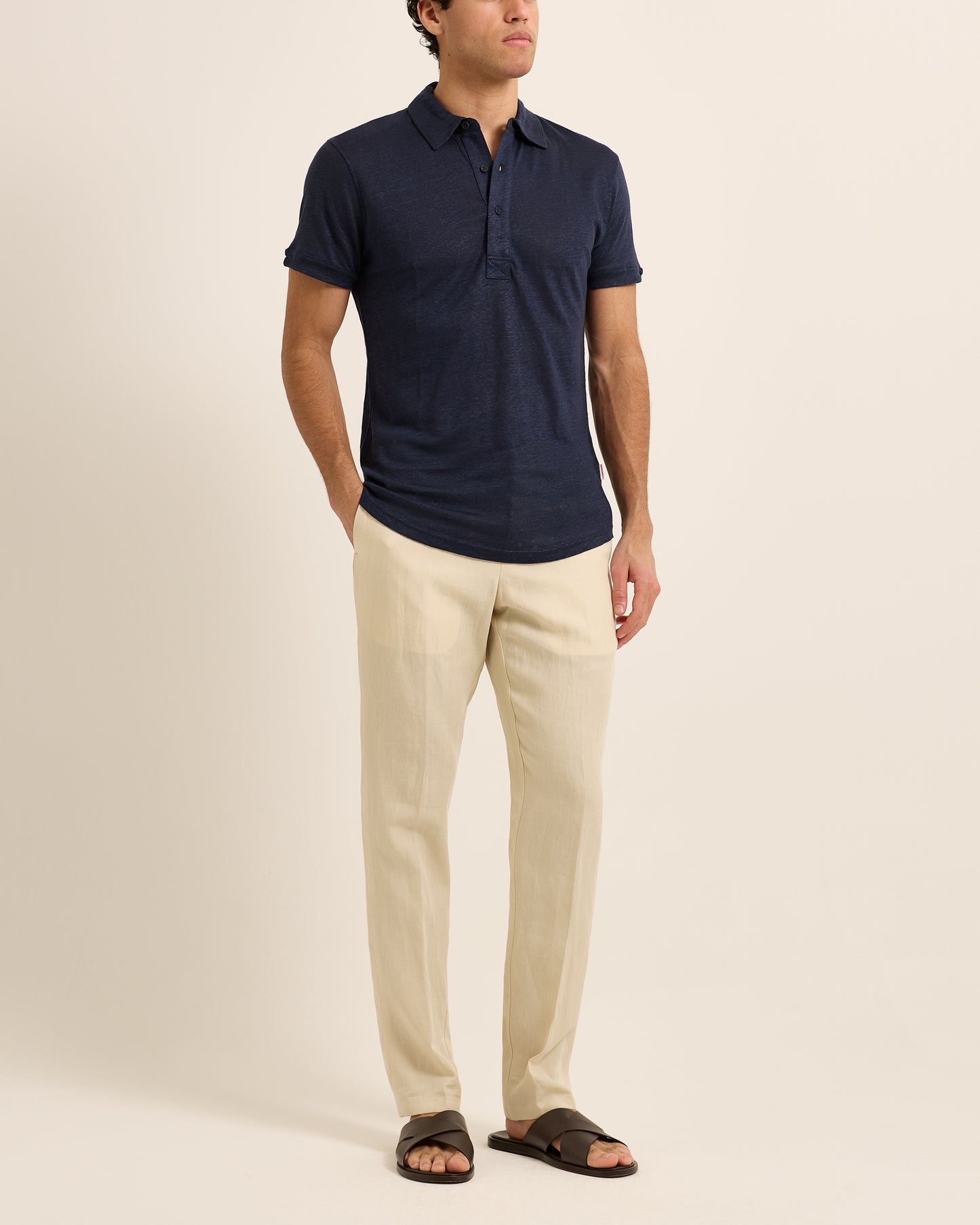 Man wearing navy polo shirt with beige trousers on a white background