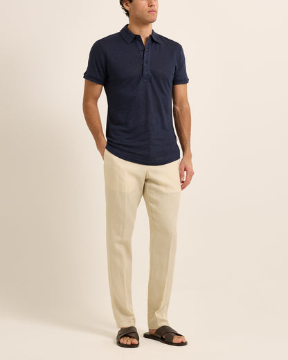 Man wearing navy polo shirt with beige trousers on a white background