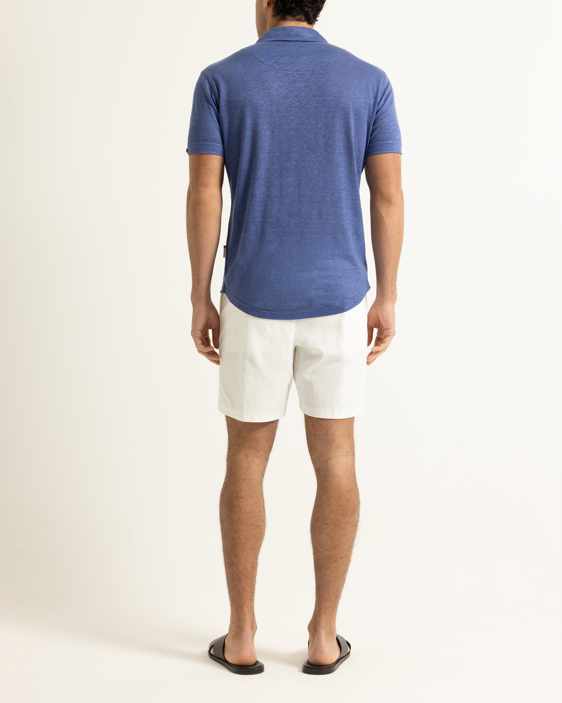 Man wearing a blue polo shirt and white shorts on a plain background