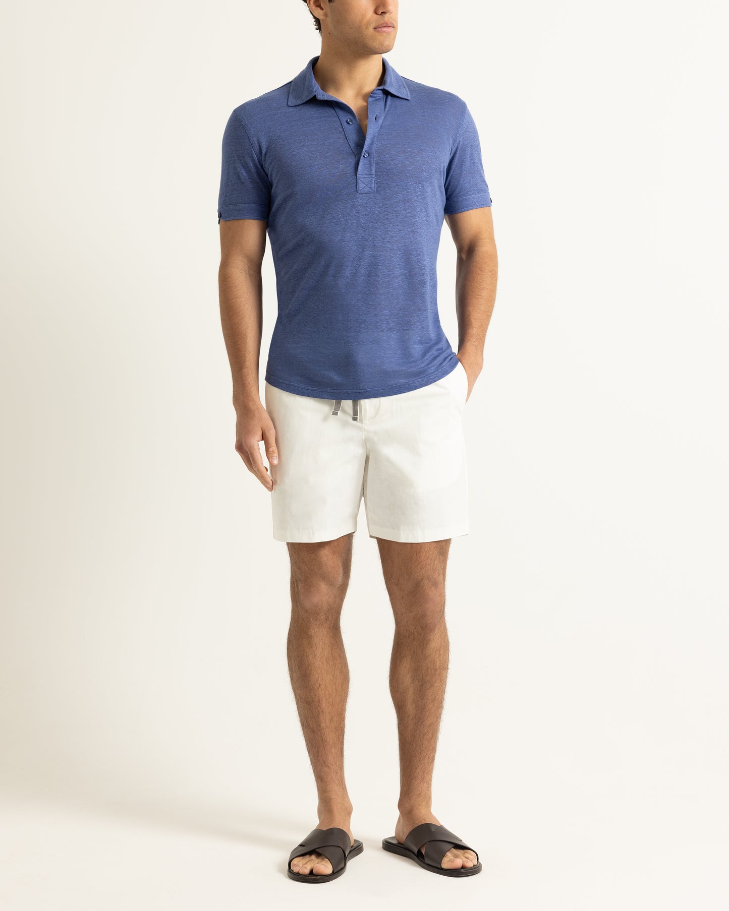 Man wearing a blue polo shirt and white shorts on a plain background