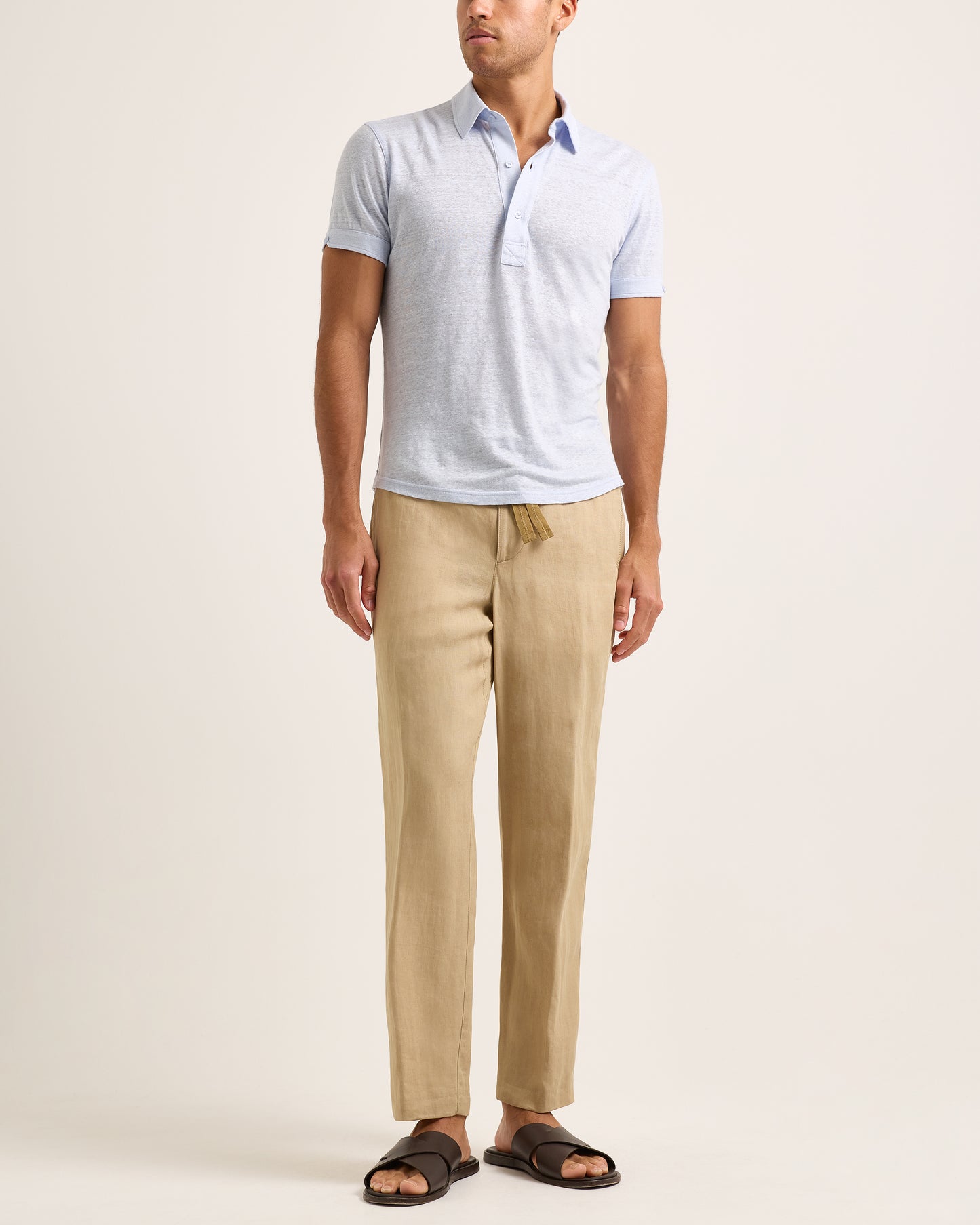 Model wearing light blue polo shirt with beige trousers on a white background