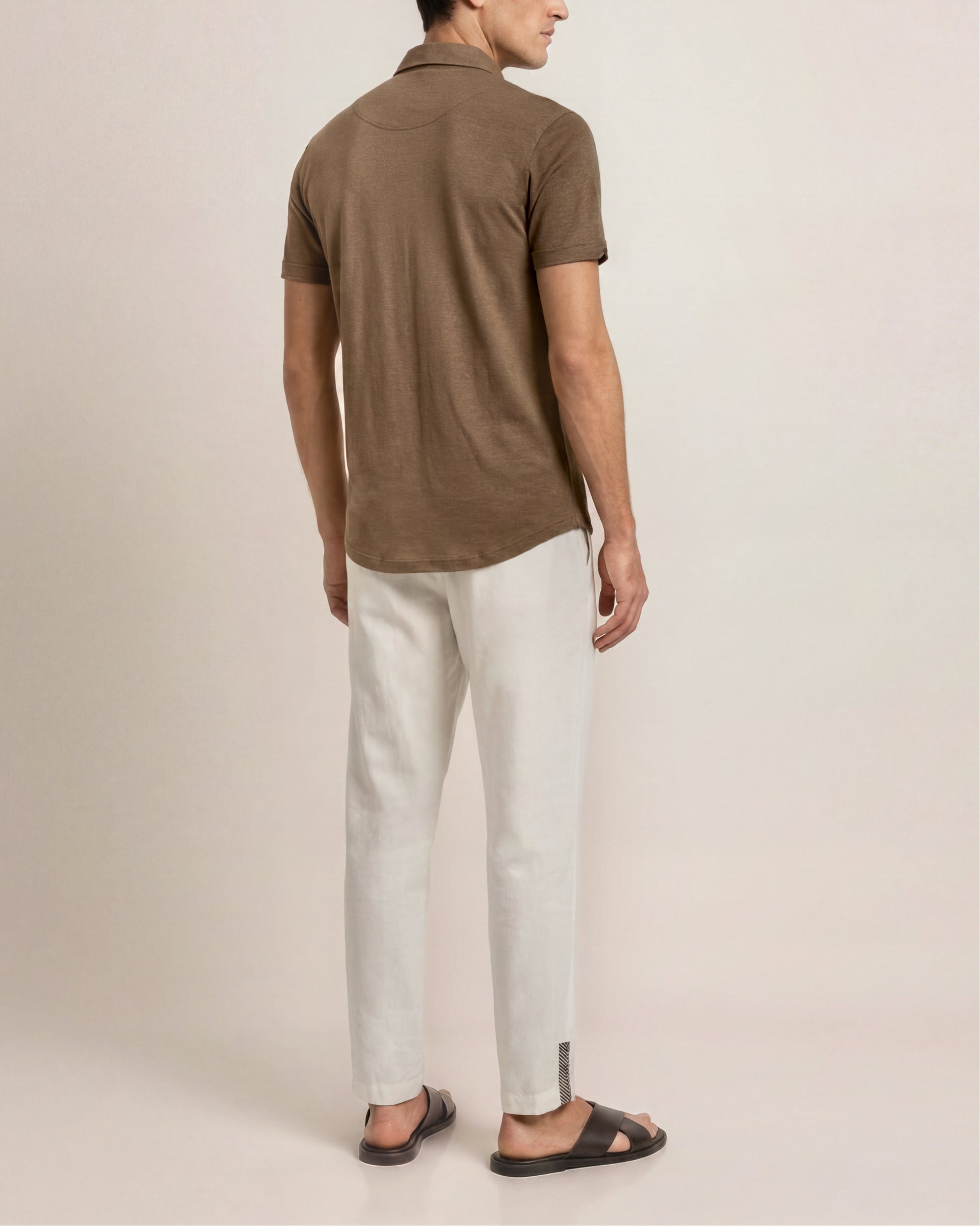 Person wearing a brown polo shirt and light-colored pants on a plain background