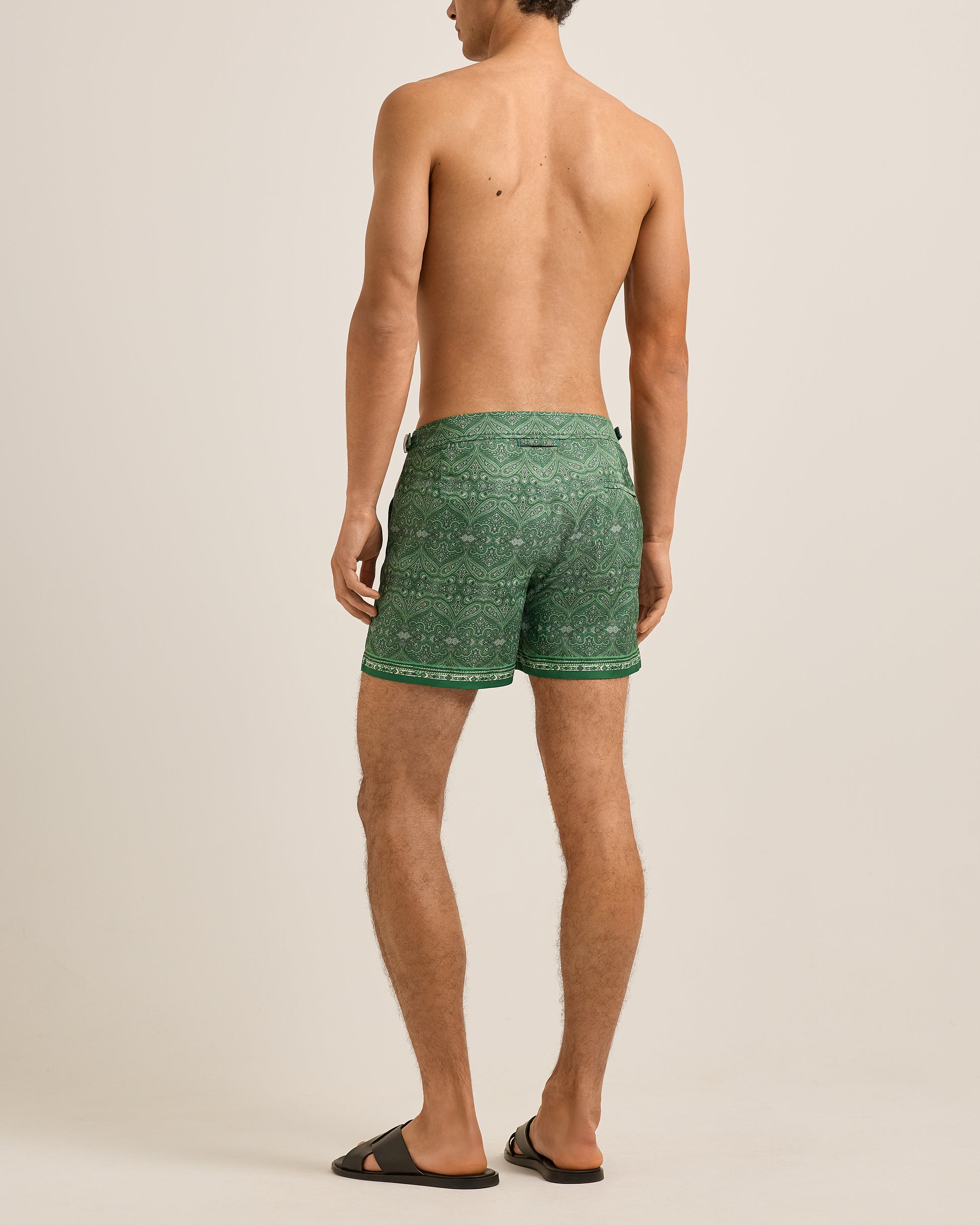 Man wearing green patterned swim shorts on a beige background