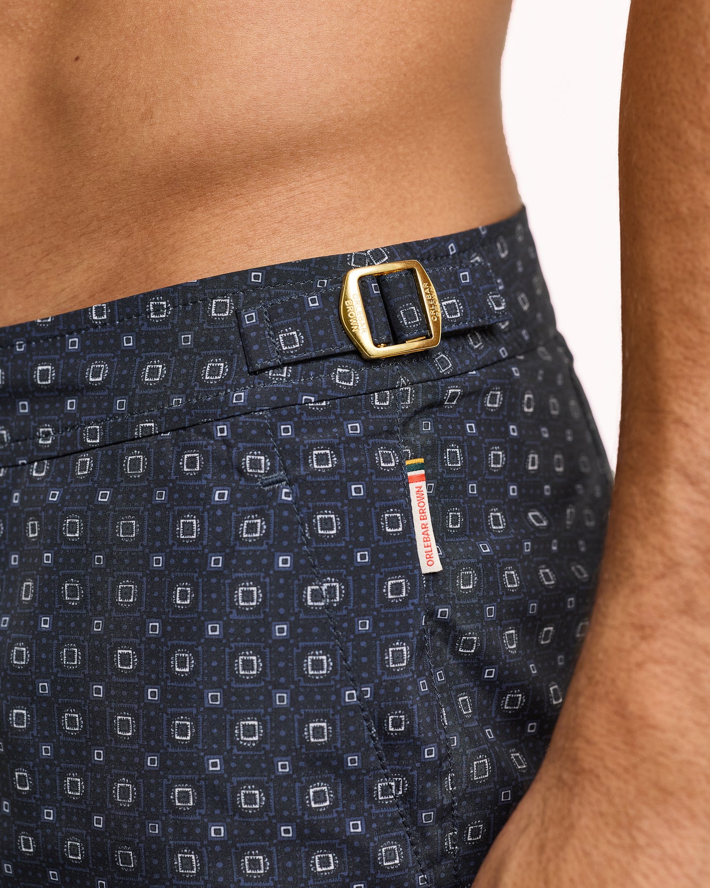 Navy patterned swim shorts with a gold buckle on a white background