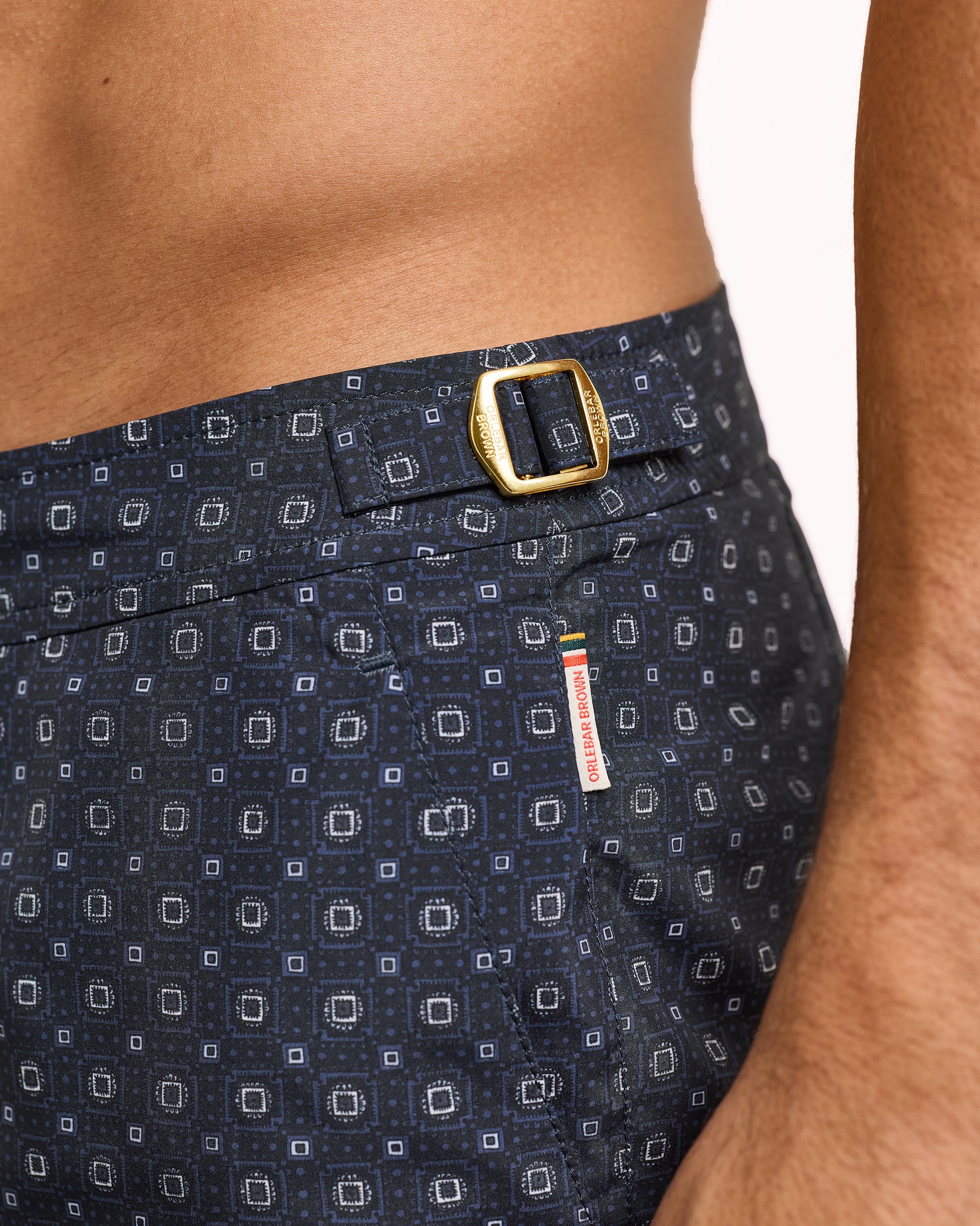 Navy patterned swim shorts with a gold buckle on a white background