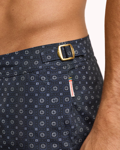 Navy patterned swim shorts with a gold buckle on a white background