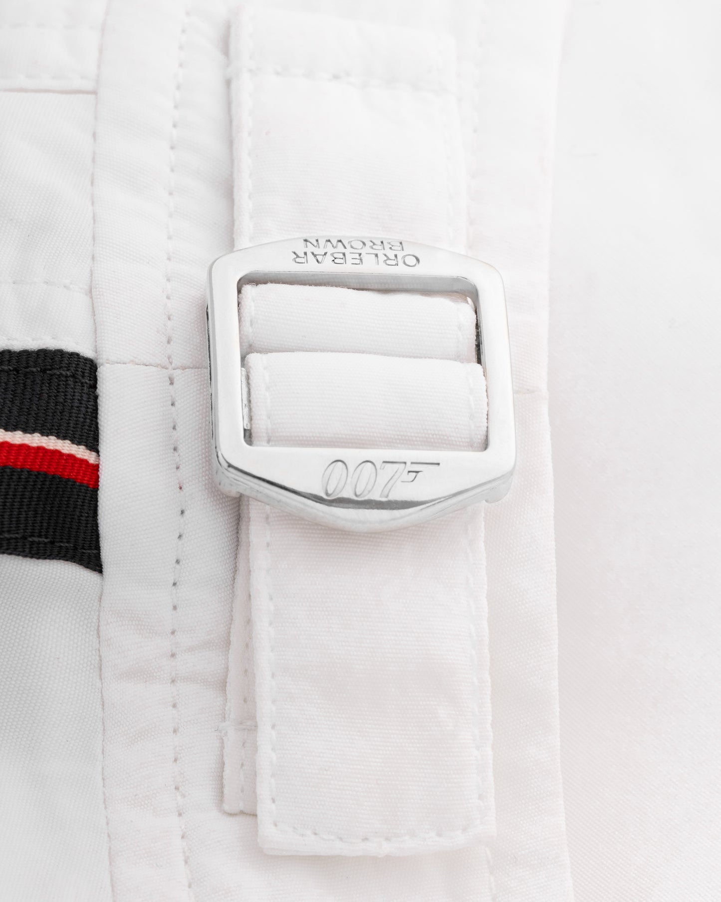 Close-up of a white jacket with a silver buckle featuring the James Bond 007 logo on a light gray background.