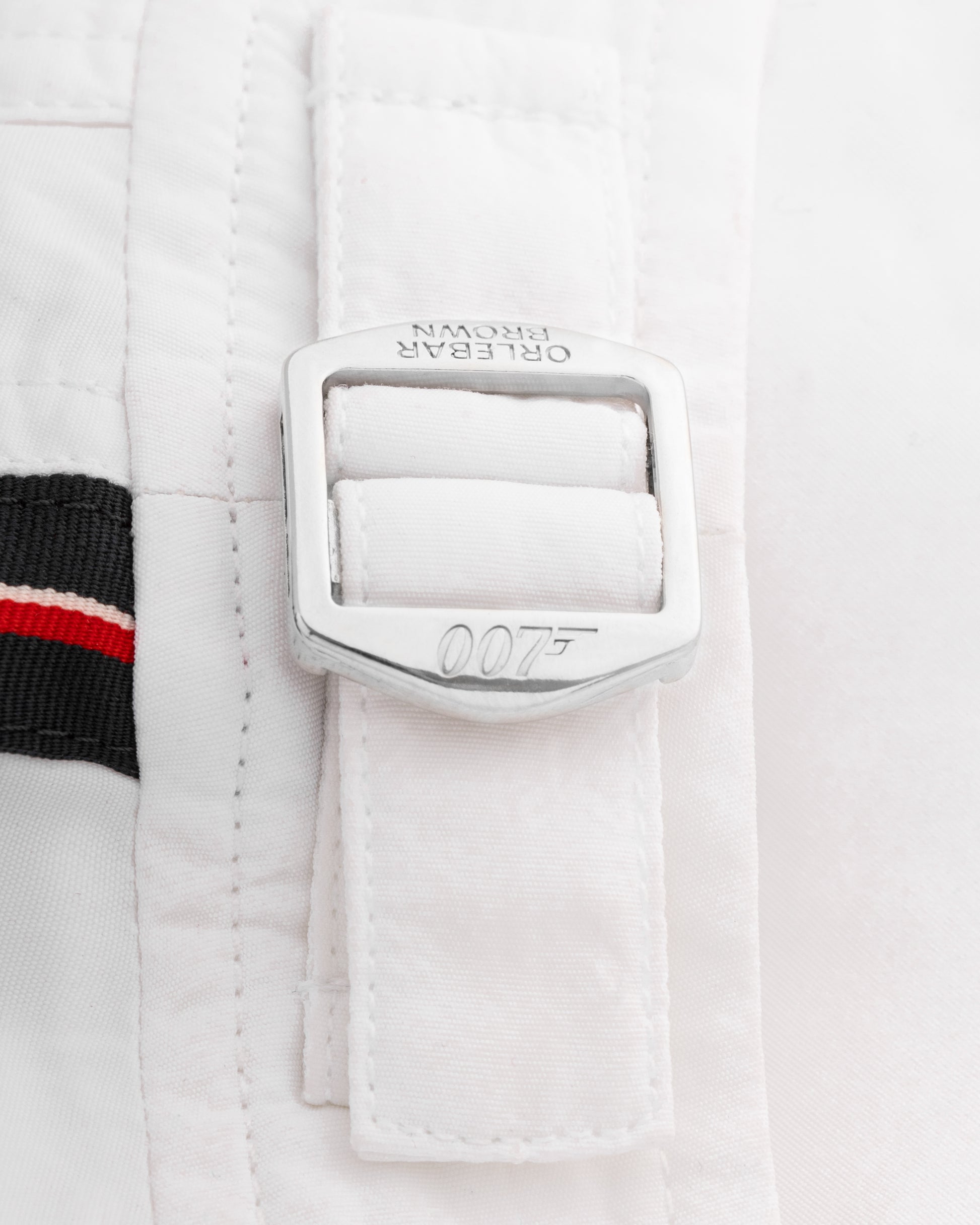 Close-up of a white jacket with a silver buckle featuring the James Bond 007 logo on a light gray background.