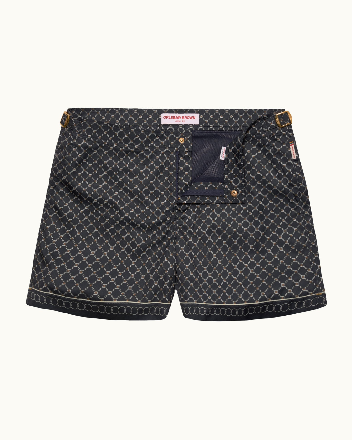 A pair of dark gray patterned swimshorts with a navy blue pocket and gold-tone hardware, shown flat on a light cream background.