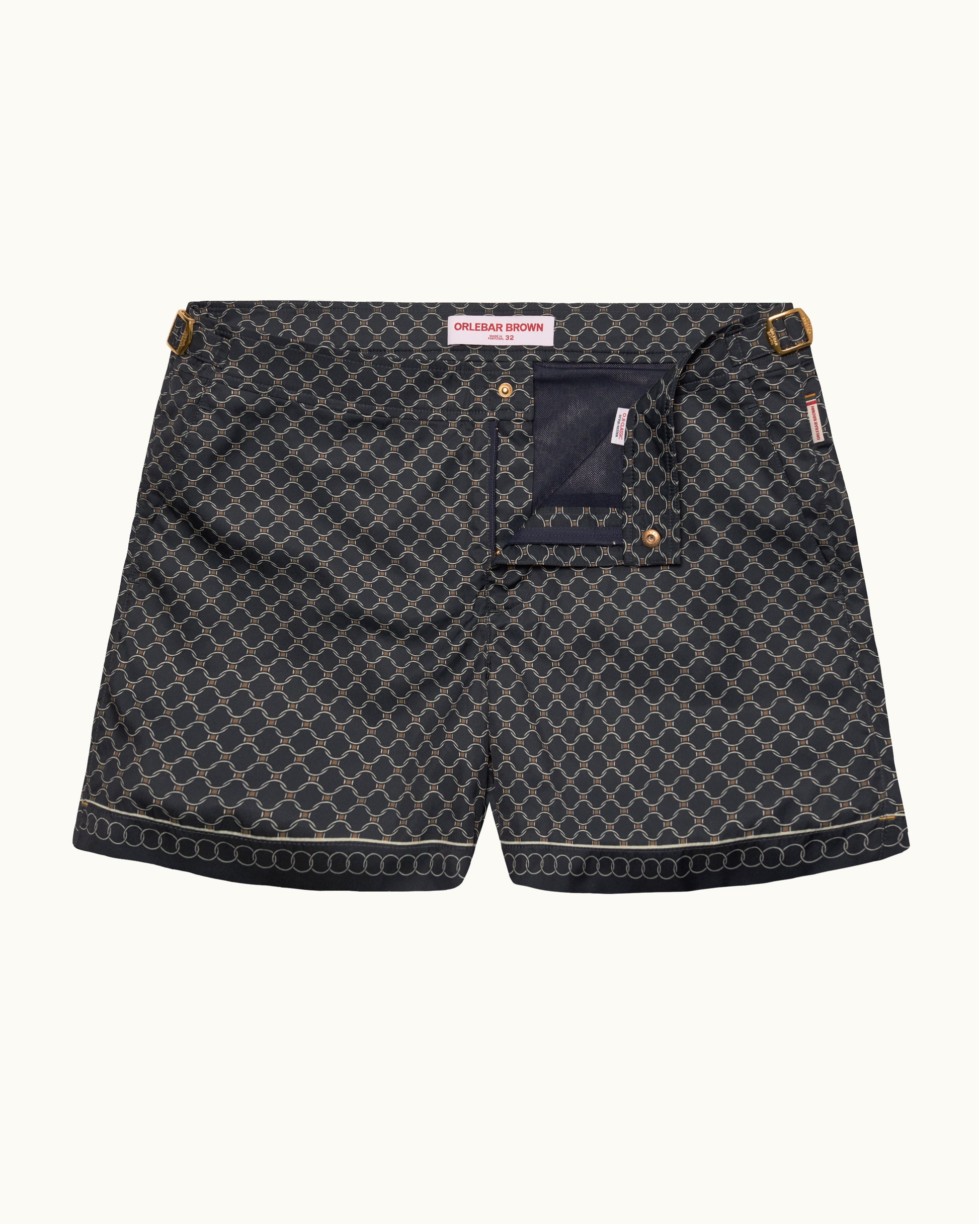 A pair of dark gray patterned swimshorts with a navy blue pocket and gold-tone hardware, shown flat on a light cream background.