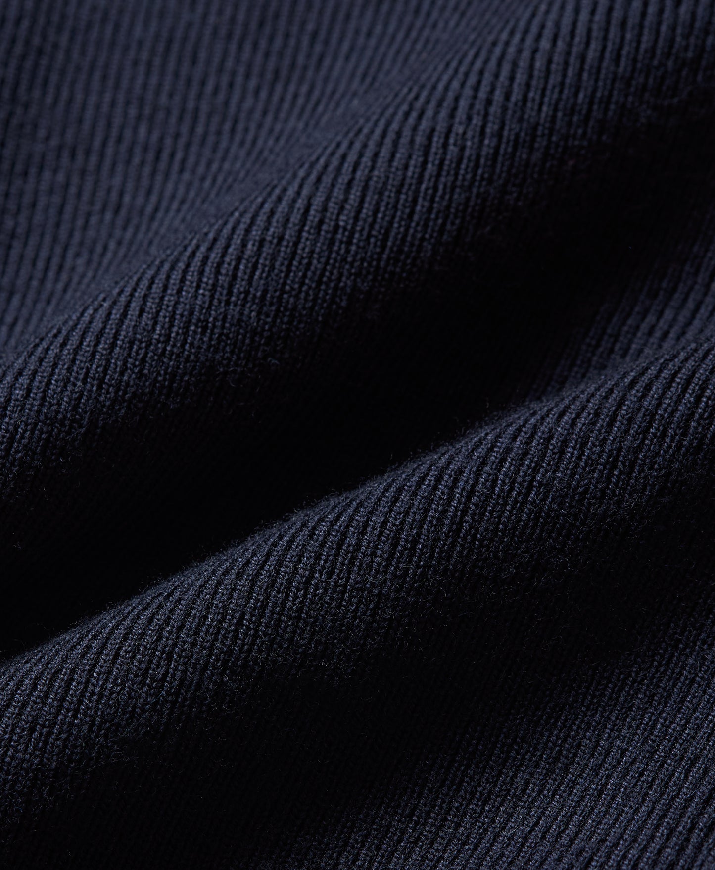 Close-up of dark navy ribbed fabric texture with soft folds and visible knit detail.