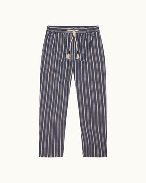 A pair of navy blue and off-white vertically striped pants with an elastic waistband and a cream-colored drawstring, against a light cream background.
