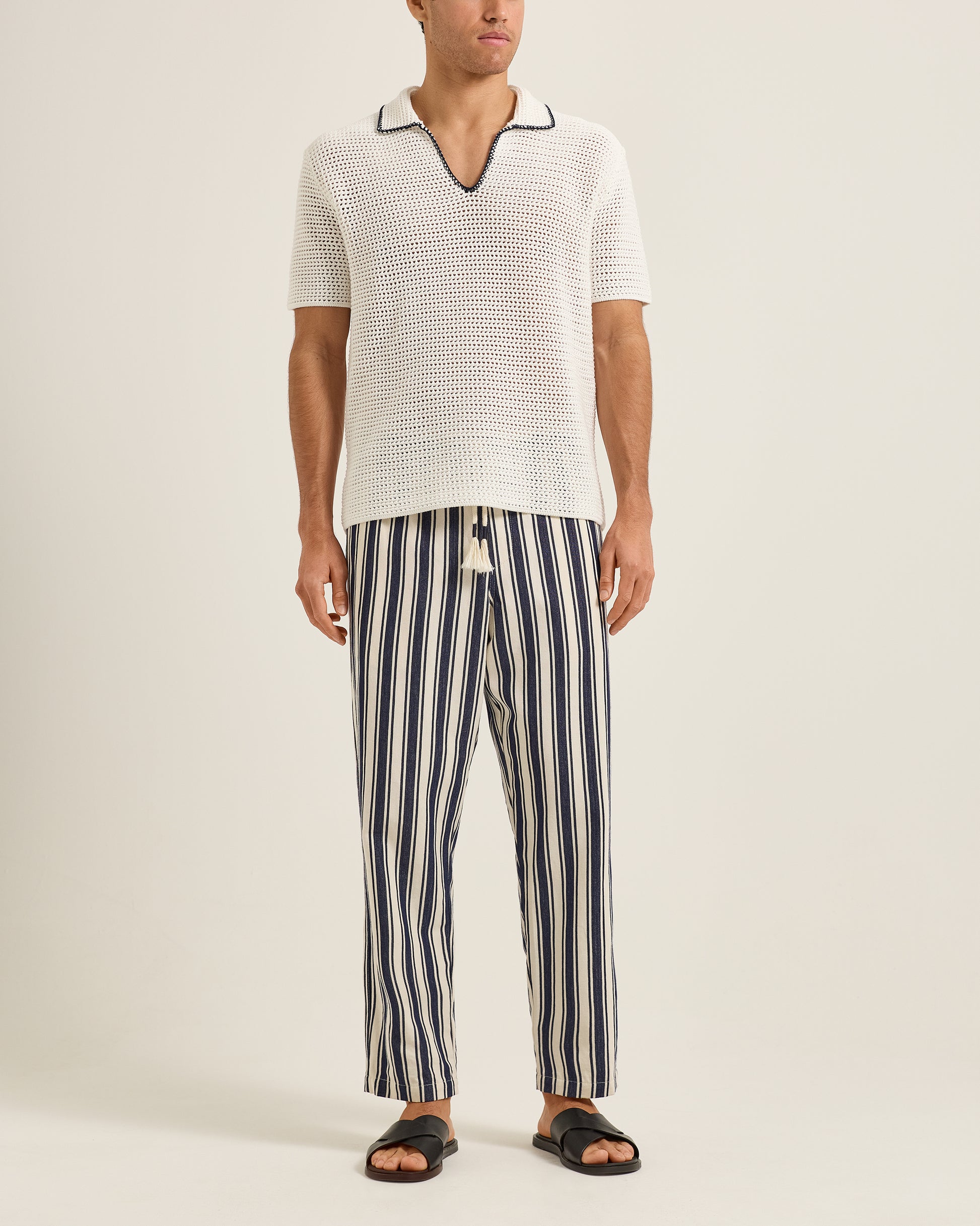 Man wearing a white textured shirt and striped pants on a plain background