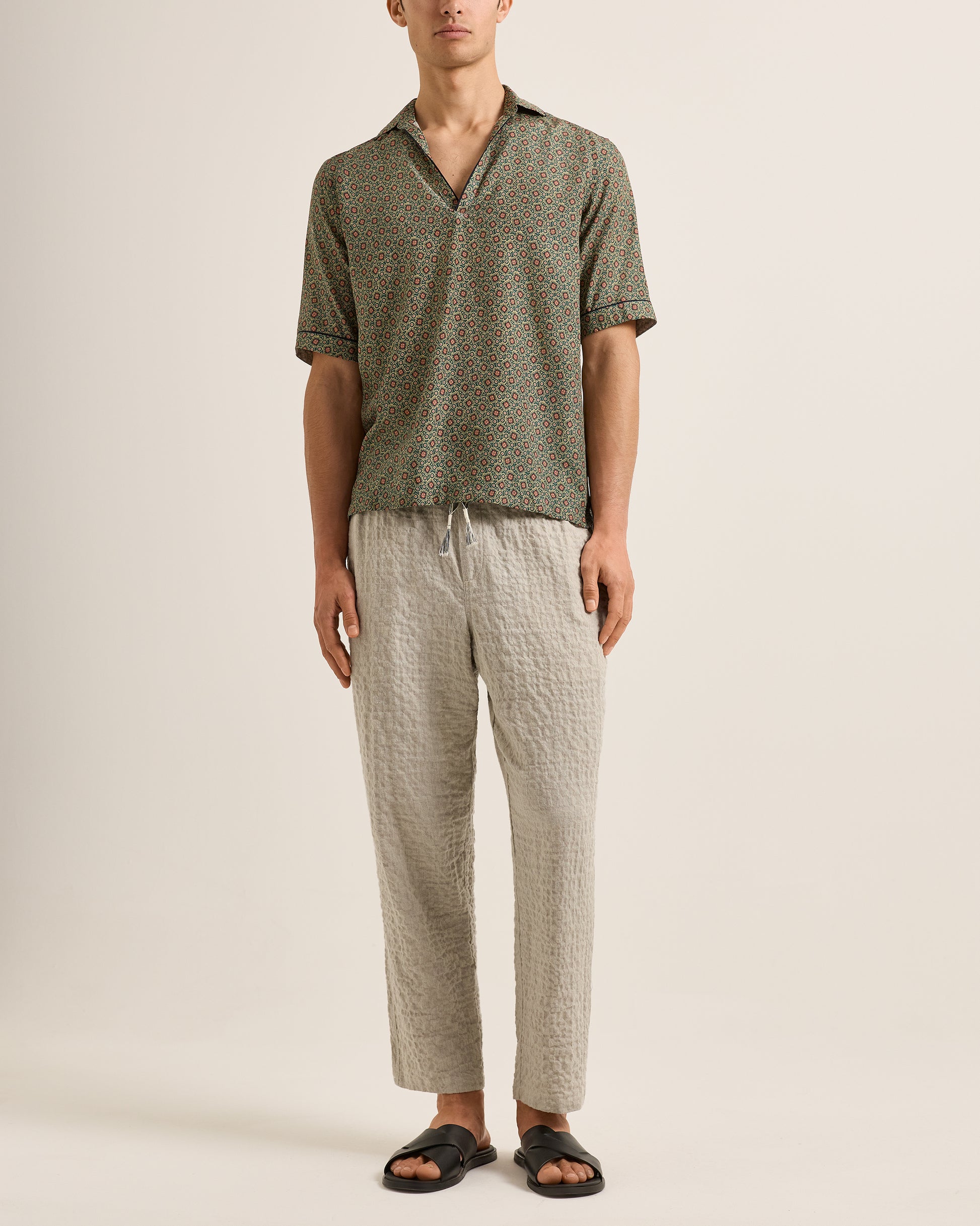 Man wearing a patterned shirt and pants on a plain background