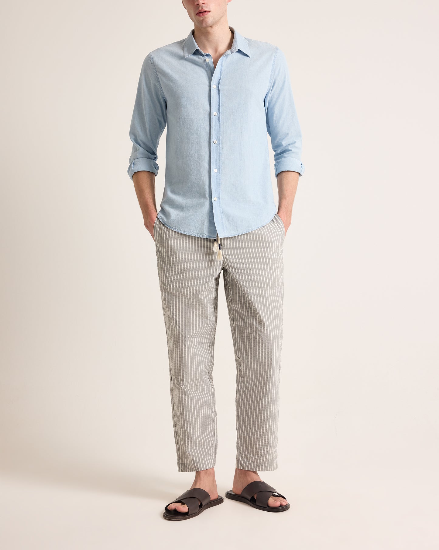 Man wearing light grey trousers with light stripe and drawstring waist, worn with a light blue shirt on a plain background