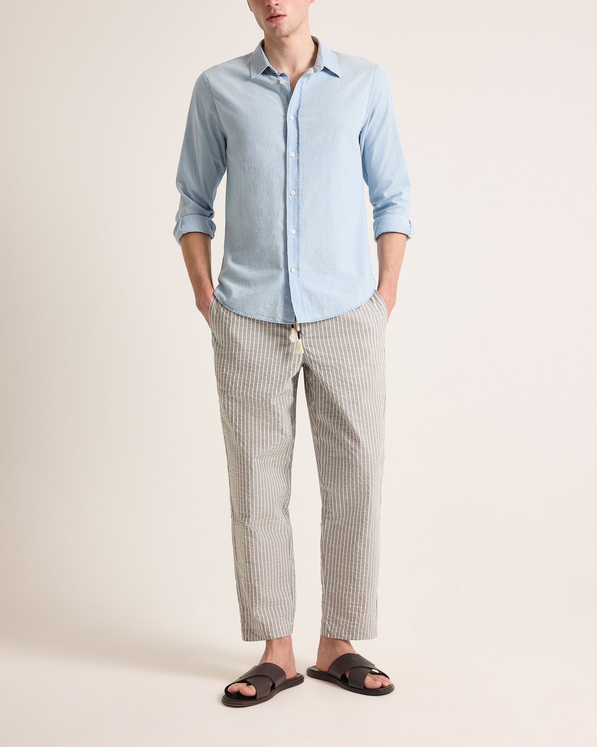 Man wearing light grey trousers with light stripe and drawstring waist, worn with a light blue shirt on a plain background