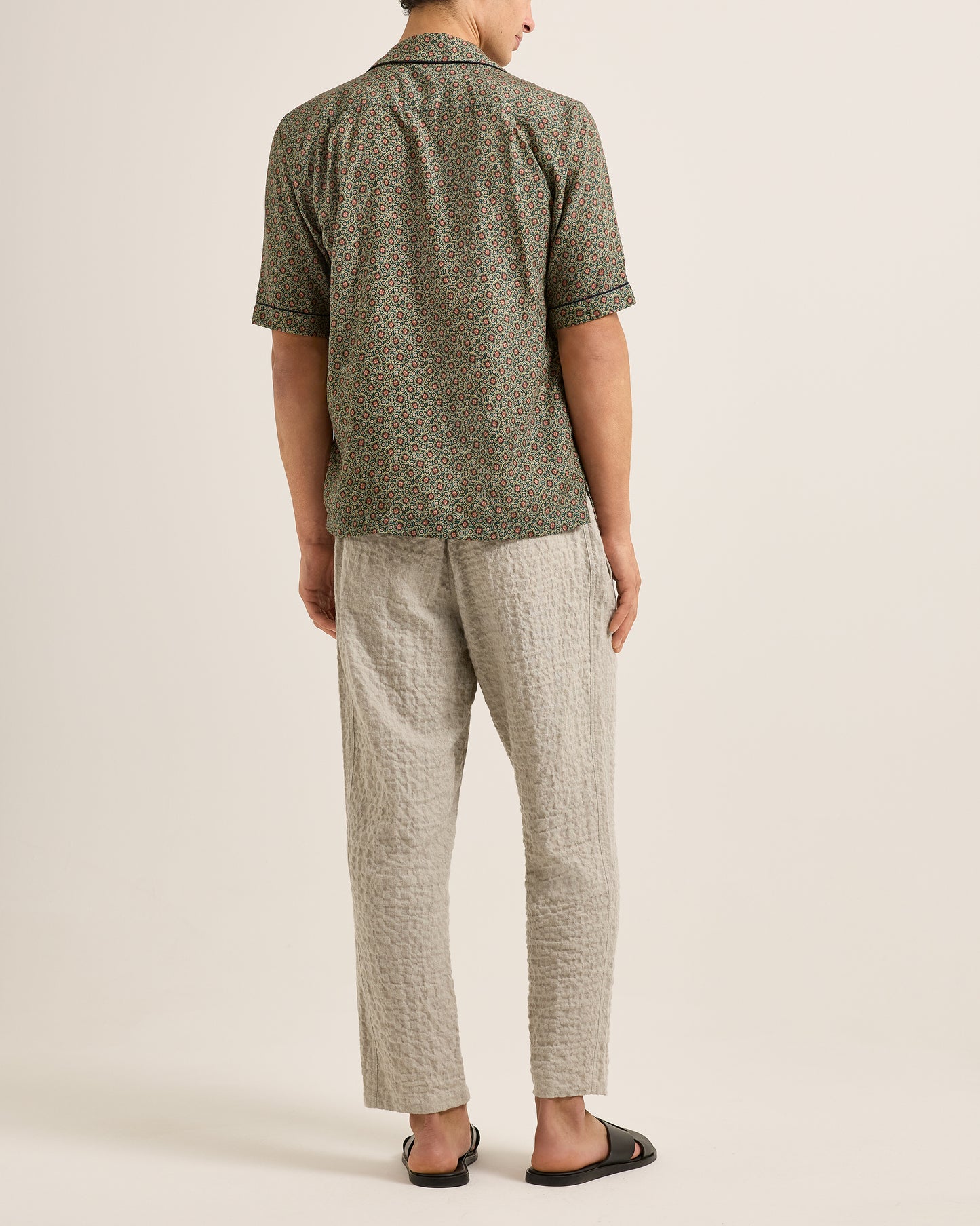 Person wearing a green patterned shirt and beige pants on a plain background