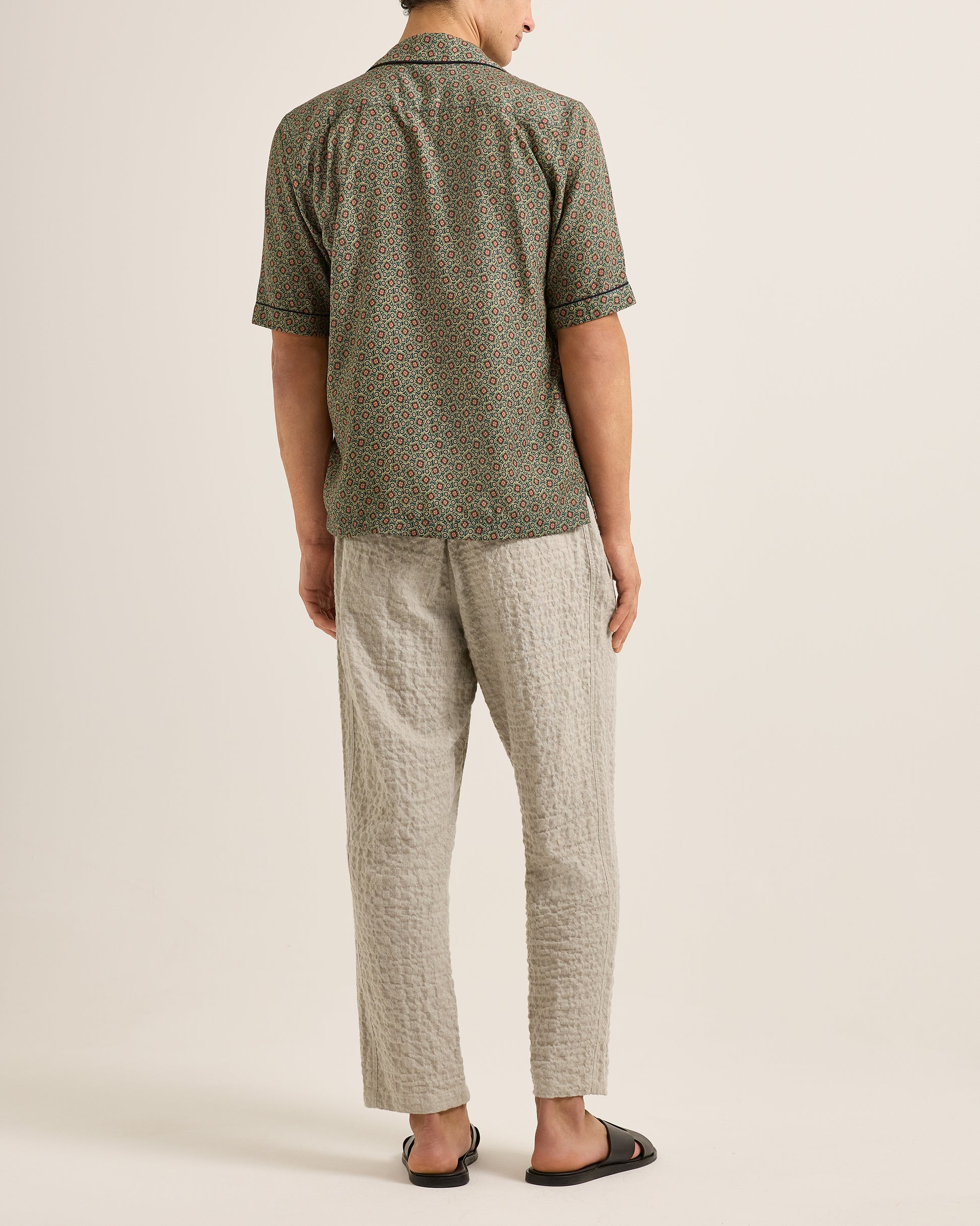 Person wearing a green patterned shirt and beige pants on a plain background