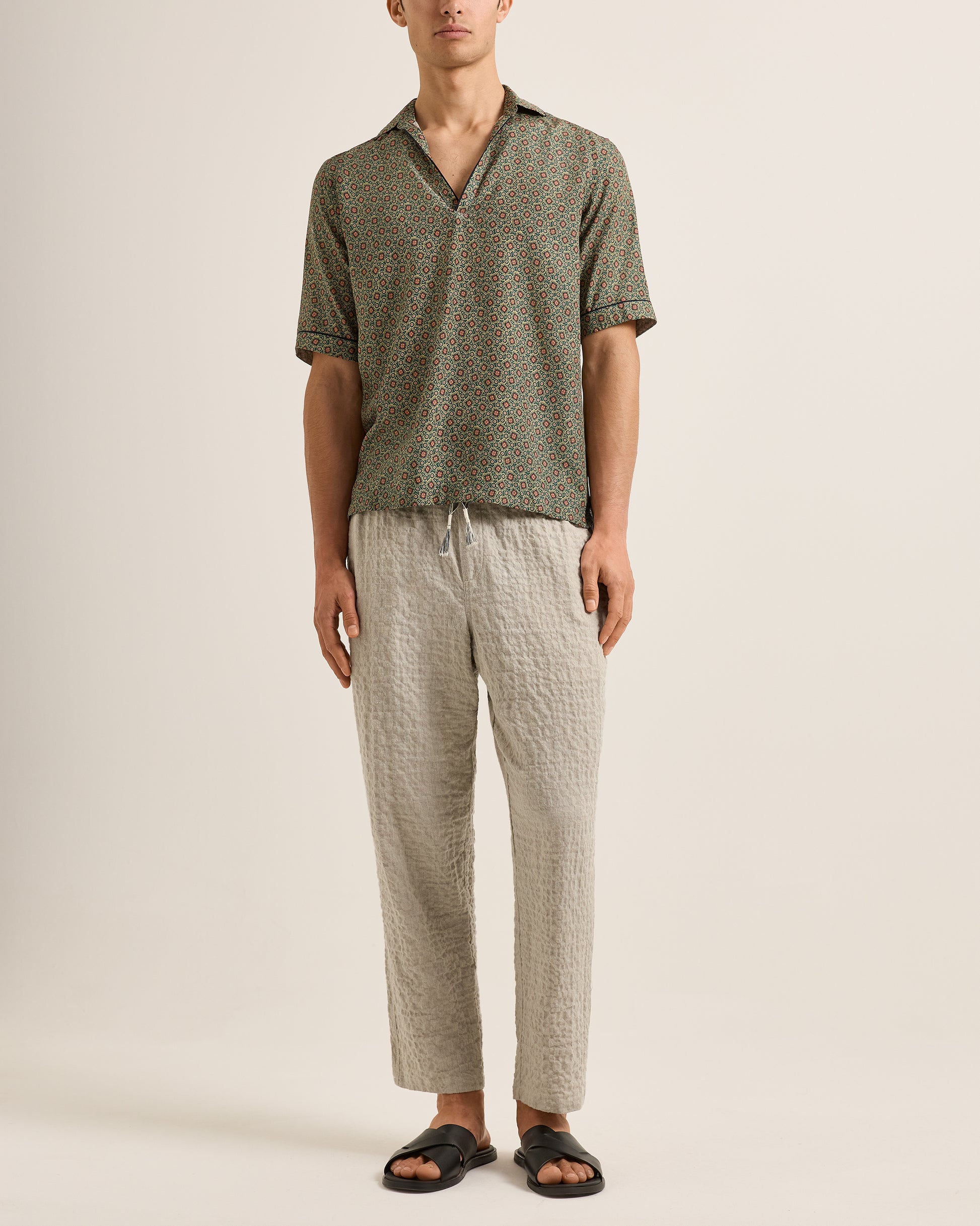 Man wearing a patterned shirt and pants on a plain background
