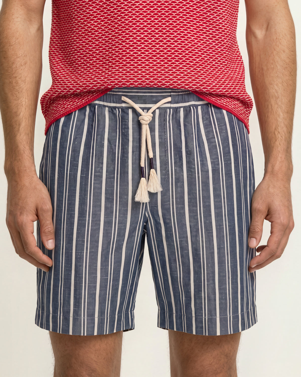 Close-up of navy-and-white striped drawcord shorts and the hem of a red patterned knit polo. on a plain background