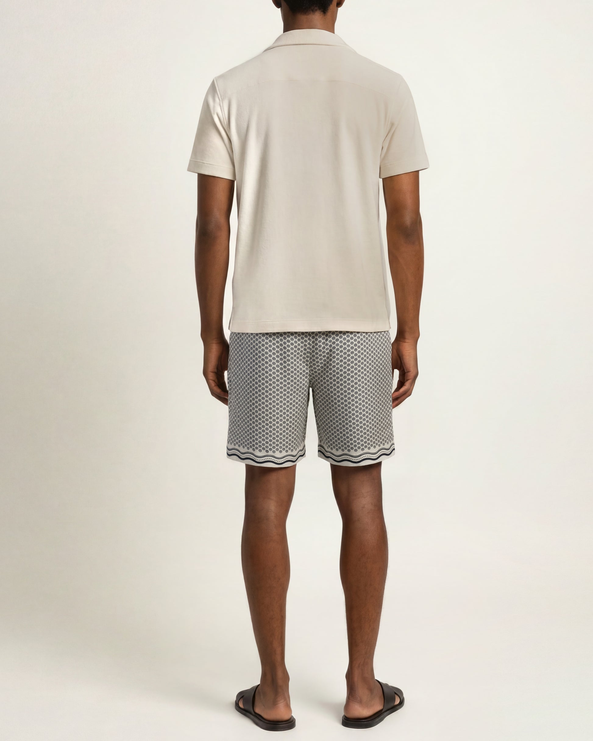 Image of the back of a model wearing white polo and printed white and navy swim shorts 