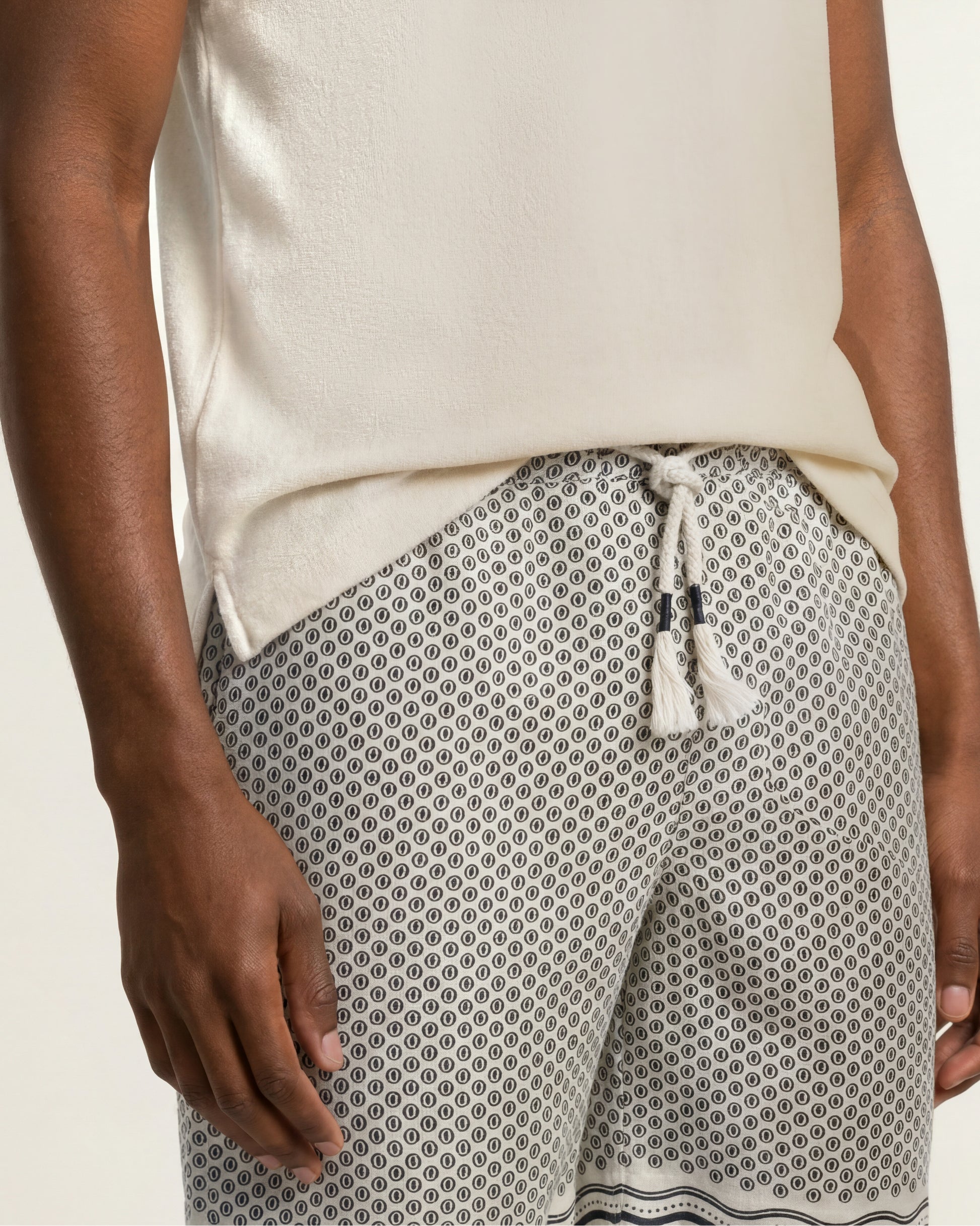 Close-up of a person wearing patterned shorts with a white drawstring and a cream sleeveless top against a light neutral background.