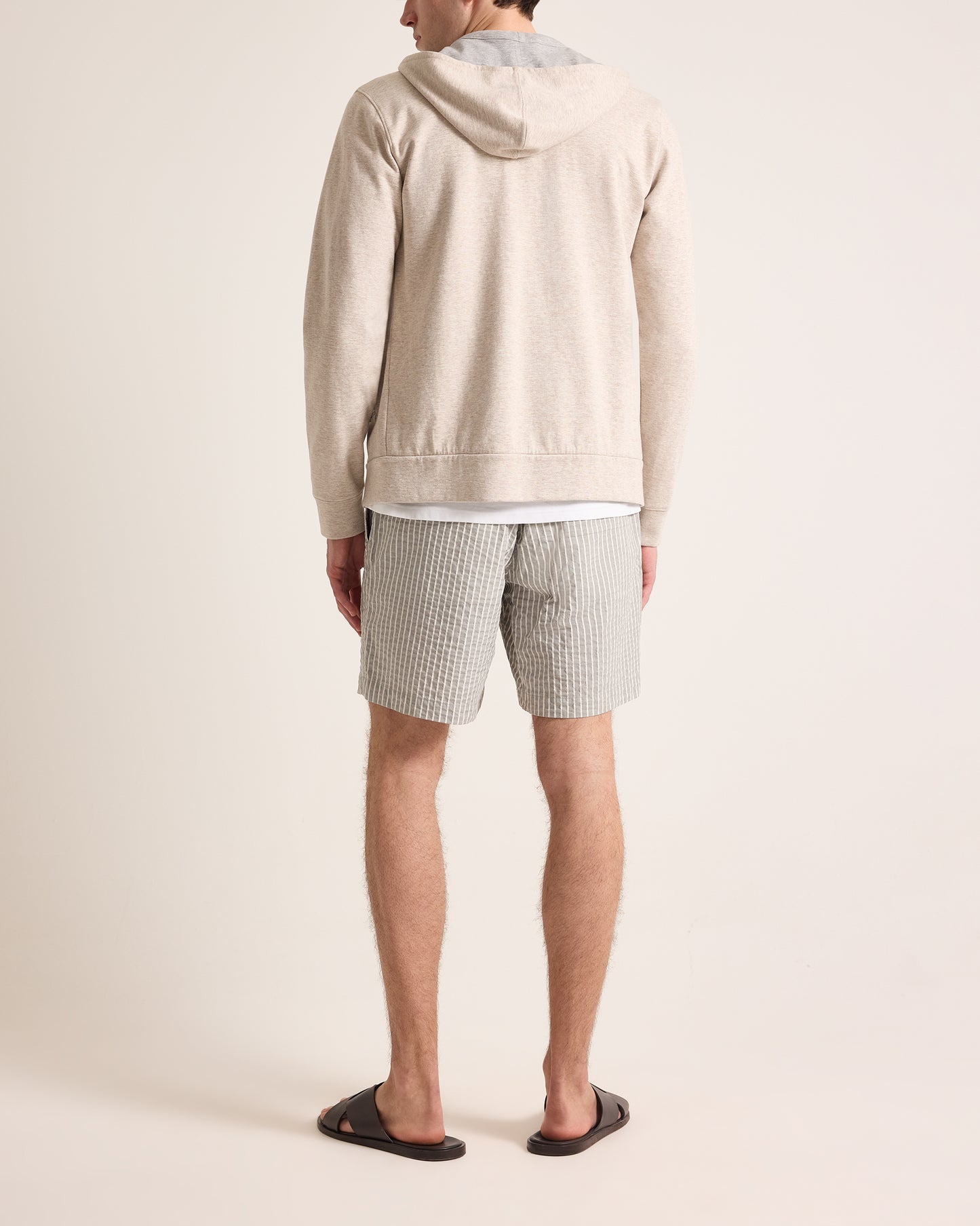Person wearing a beige hoodie and striped shorts on a plain background