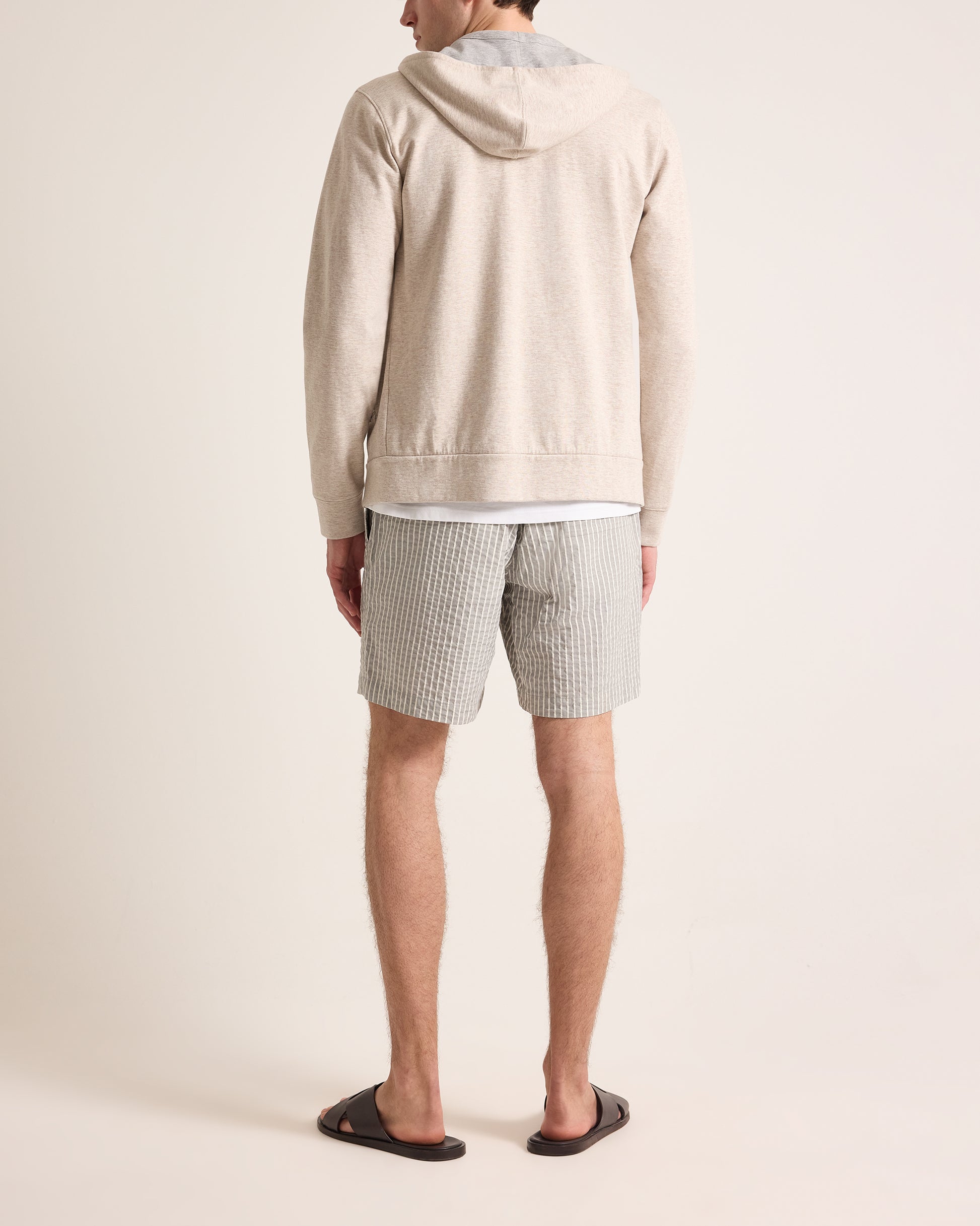 Person wearing a beige hoodie and striped shorts on a plain background