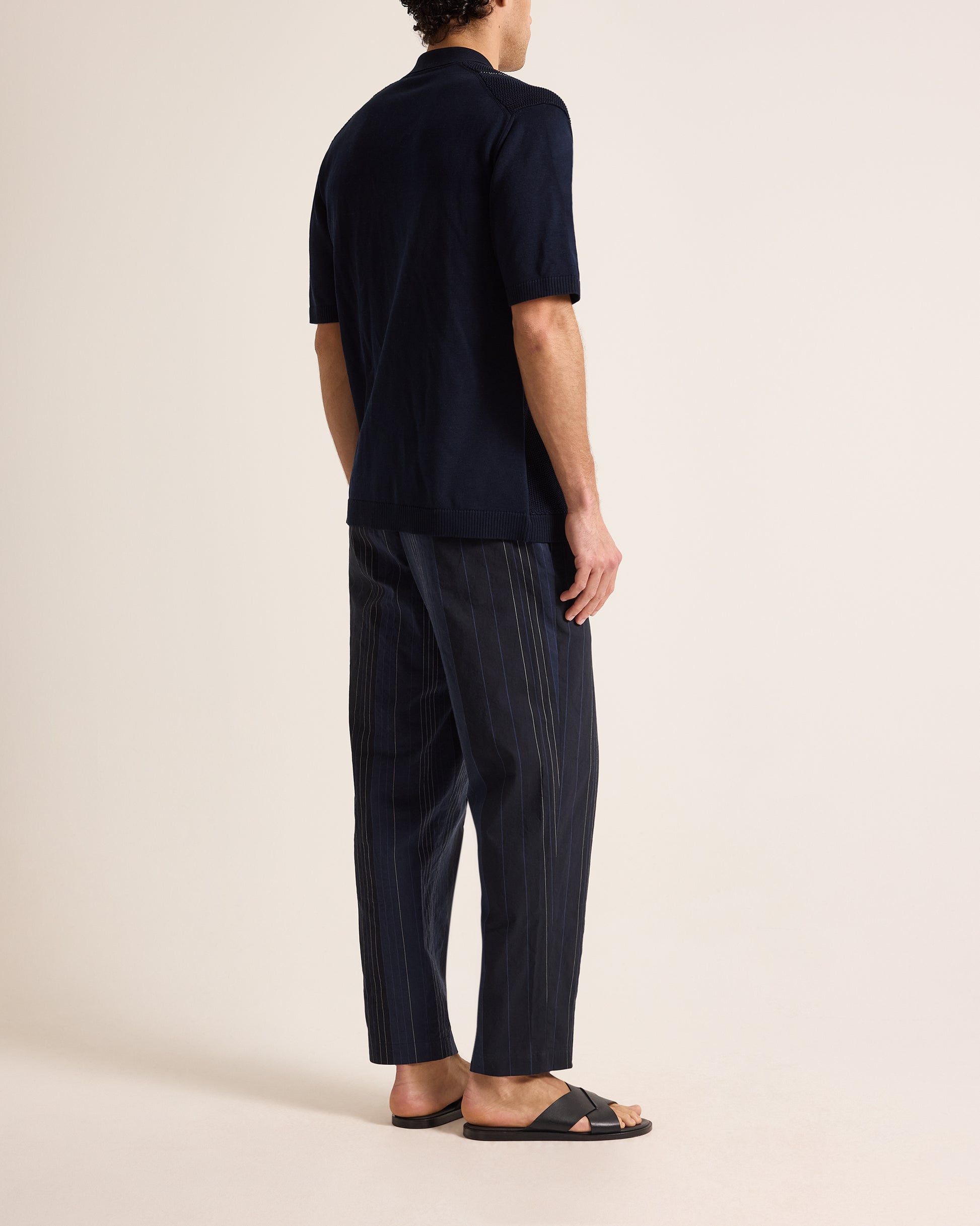 Person wearing a navy polo shirt and pinstripe pants on a beige background