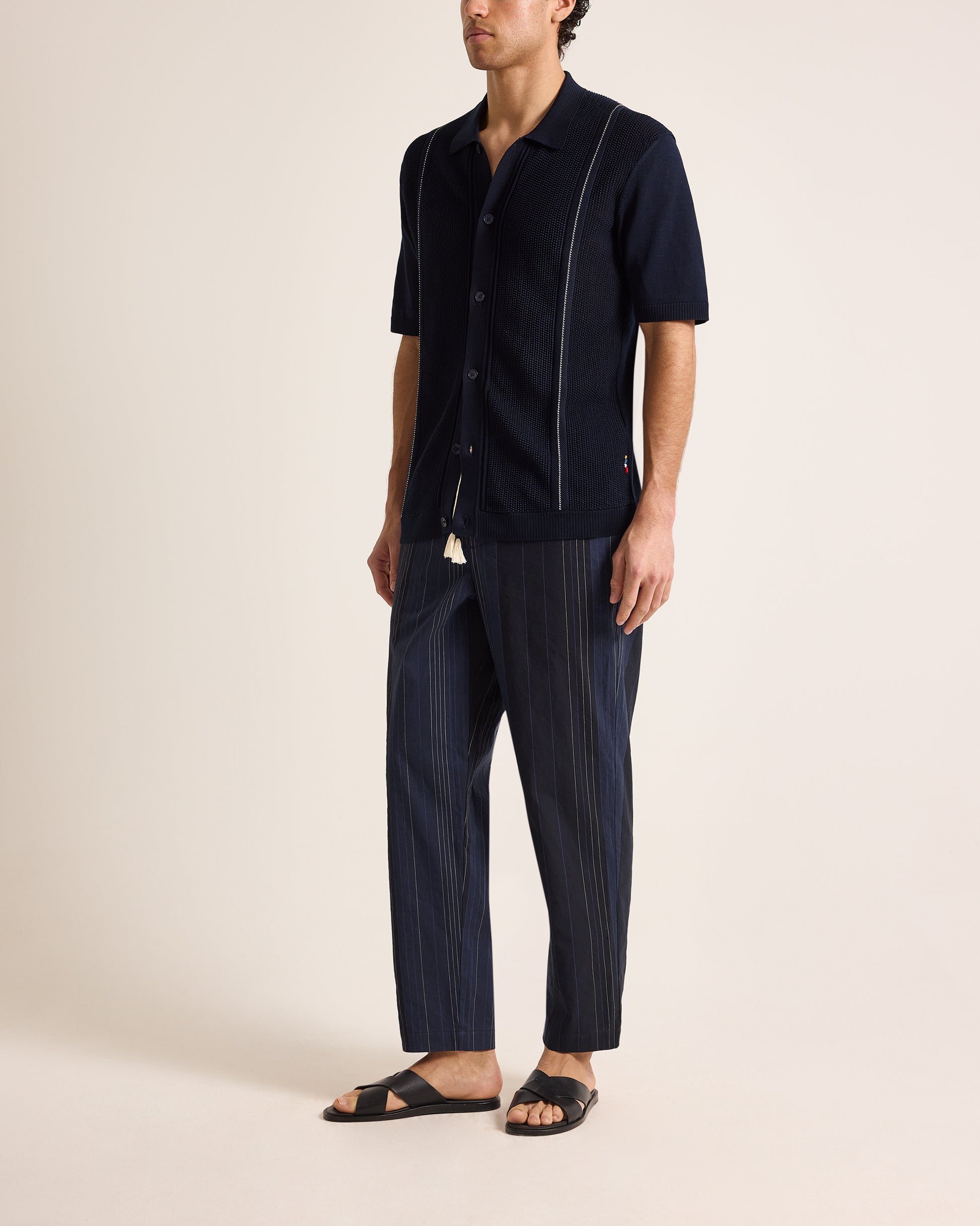 Person wearing a navy blue shirt and striped pants on a beige background